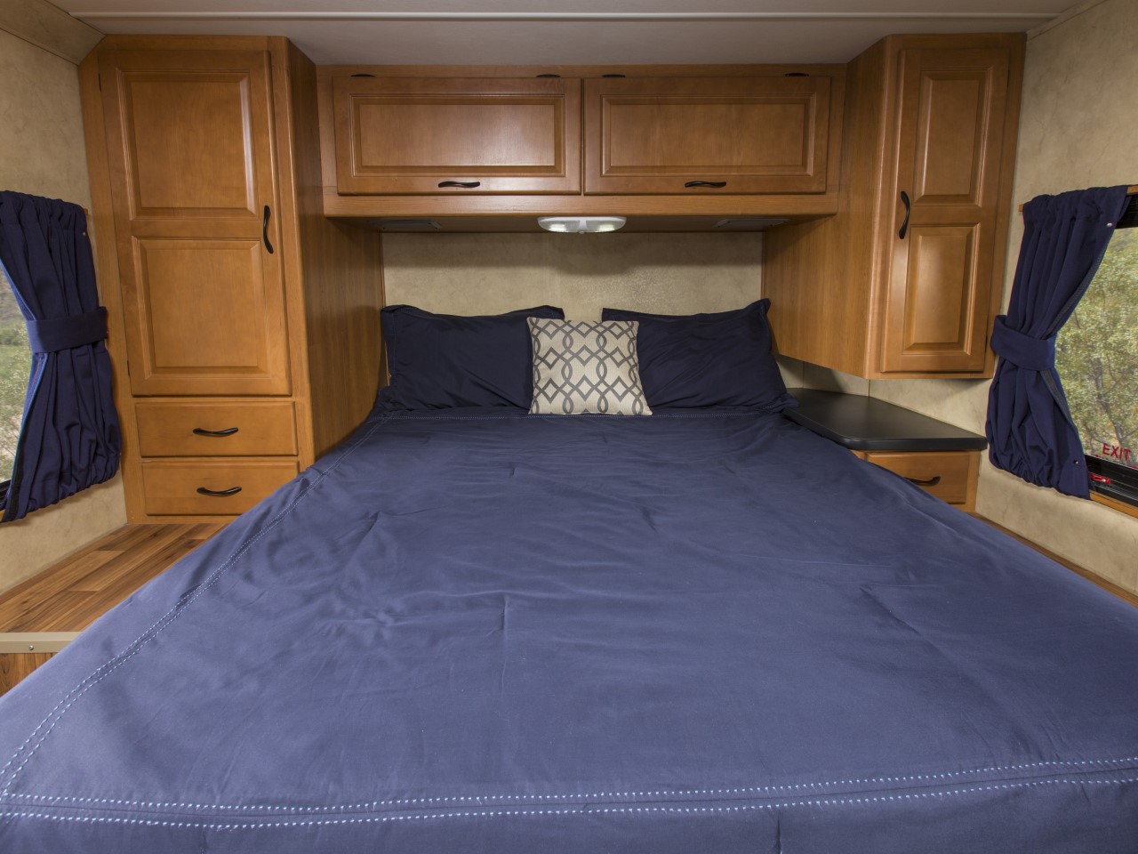 Comfortable RV rental bedroom: large bed with blue bedding, wood cabinets, and tied-back curtains revealing nature outside.. Thor Majestic 2013