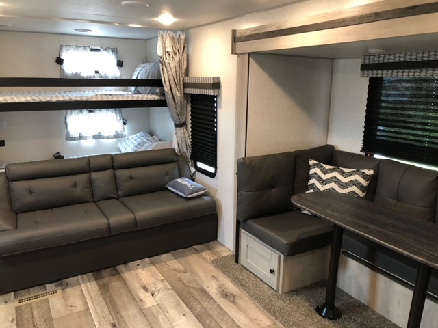 Spacious RV rental interior with comfortable bunk beds, a large sofa, and a dinette featuring corner seating and a table.. Connect SE 2021
