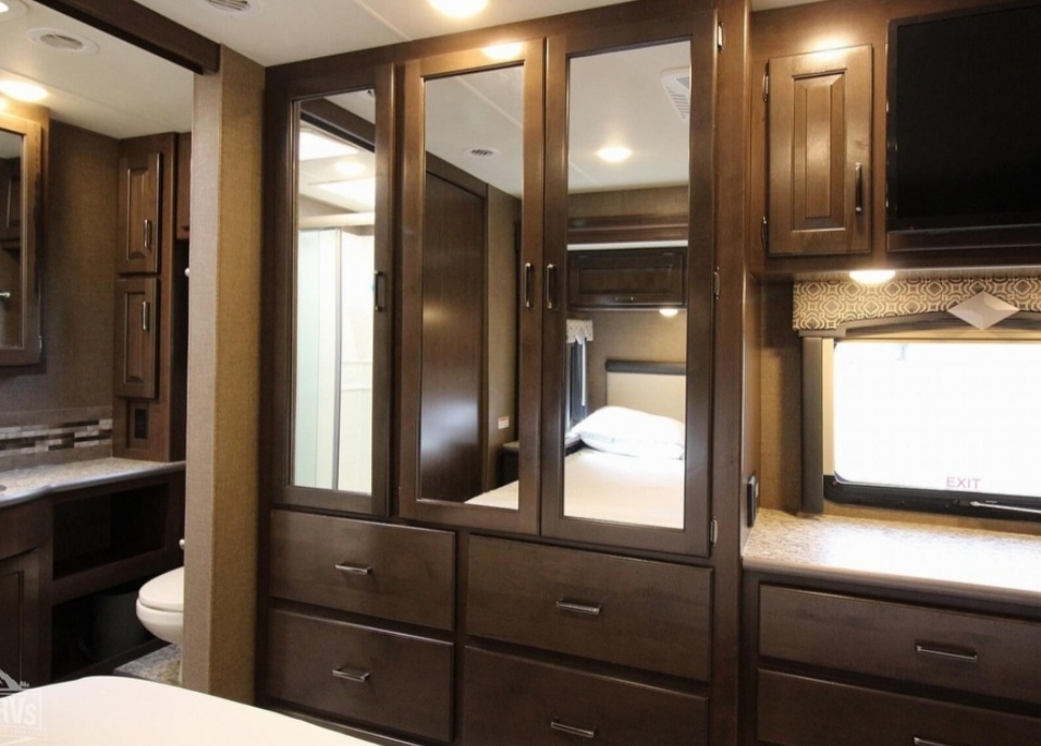 Explore this RV rental's bedroom, featuring a mirrored wardrobe, dresser, TV, and reflected bathroom amenities.. Thor Hurricane 2019
