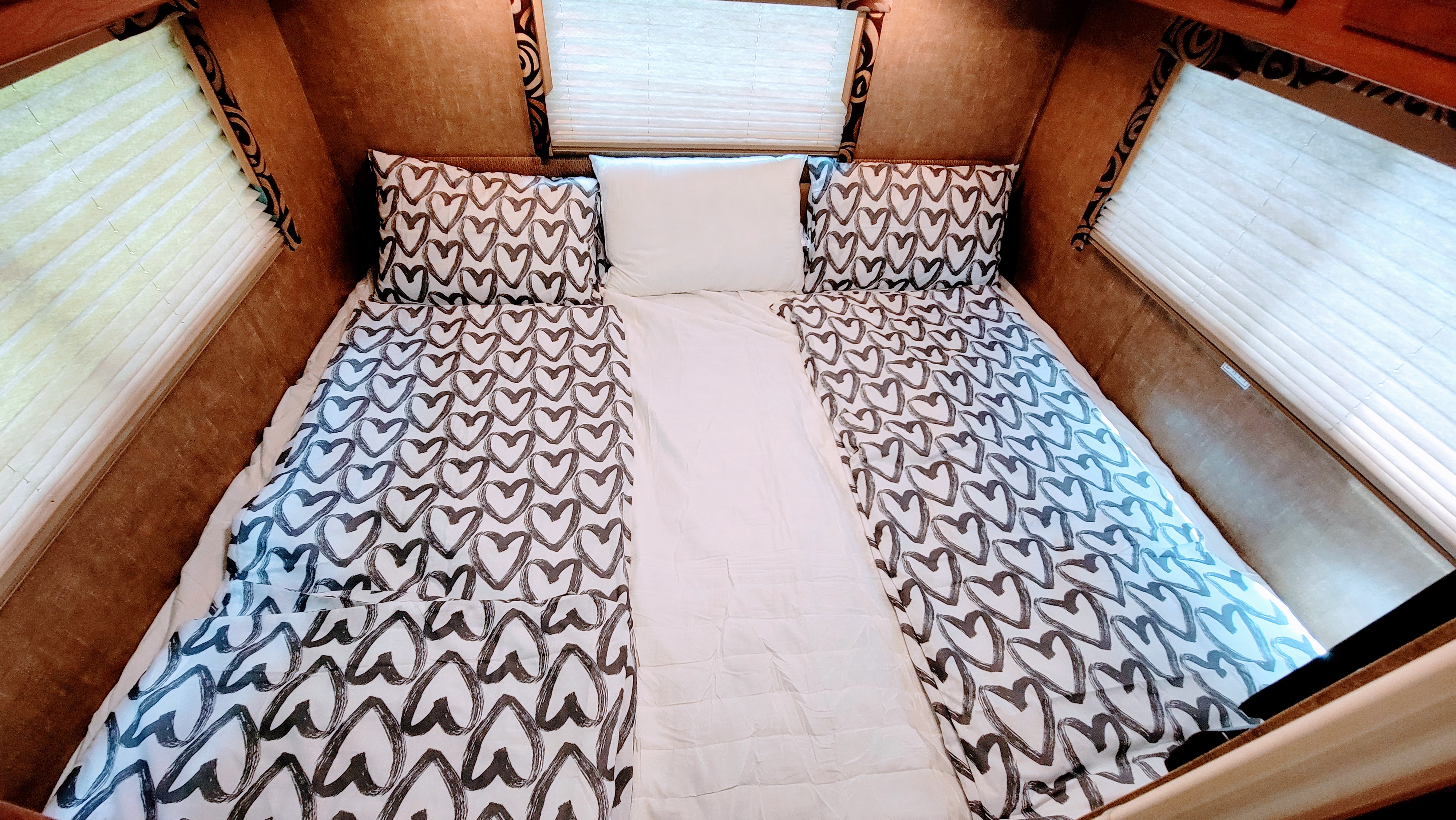 Comfortable RV rental bedroom with white and heart-patterned bedding and pleated window blinds.. Thor Vegas 2014
