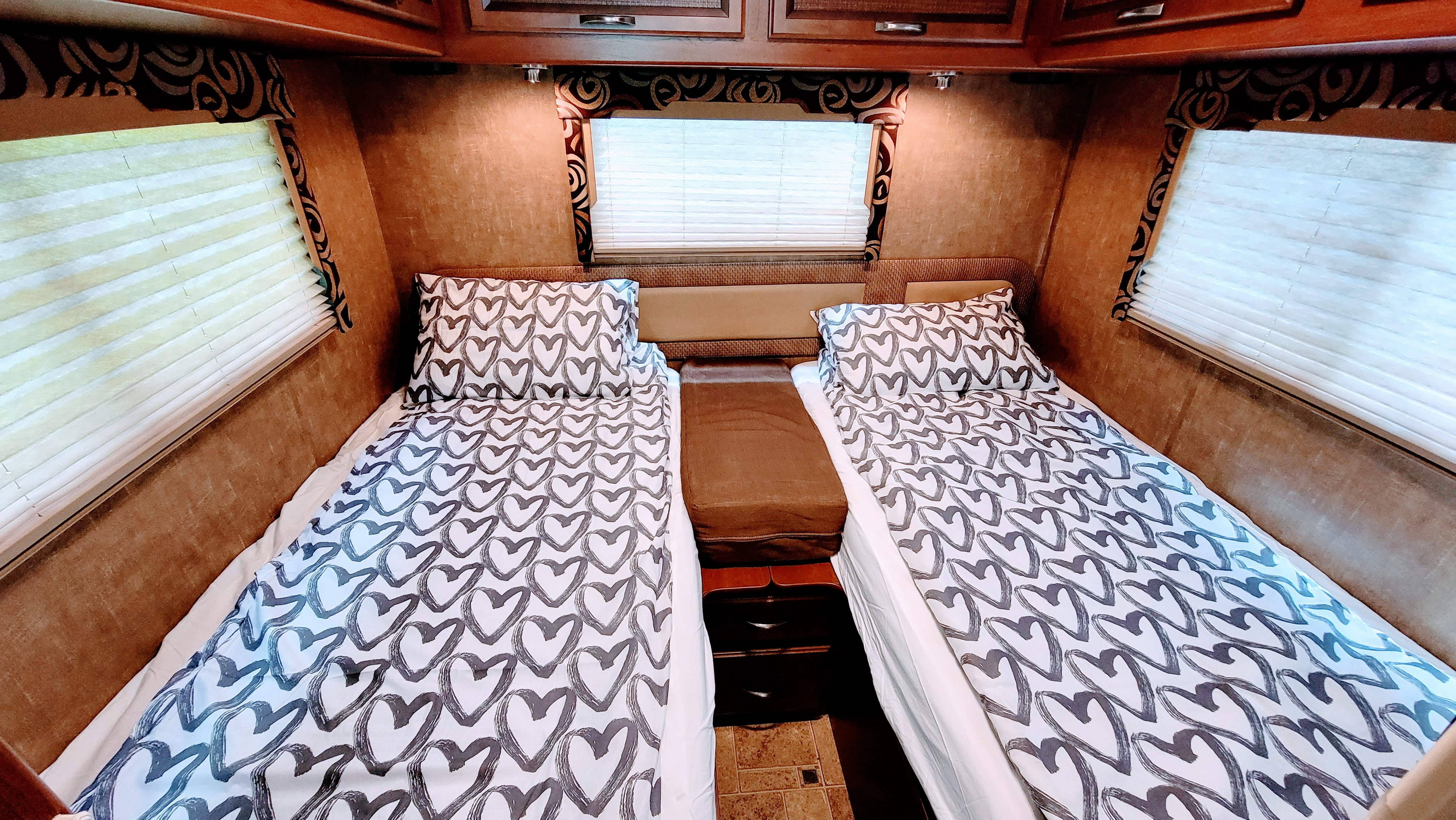 Inside an RV rental: two neatly made beds with playful heart-patterned bedding, flanked by windows & wood cabinets.. Thor Vegas 2014