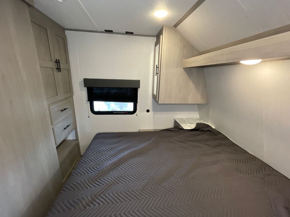 RV rental bedroom with a comfy bed, window, built-in wardrobe, and overhead storage. Compact interior for travel.. Coleman 270TQ 2022