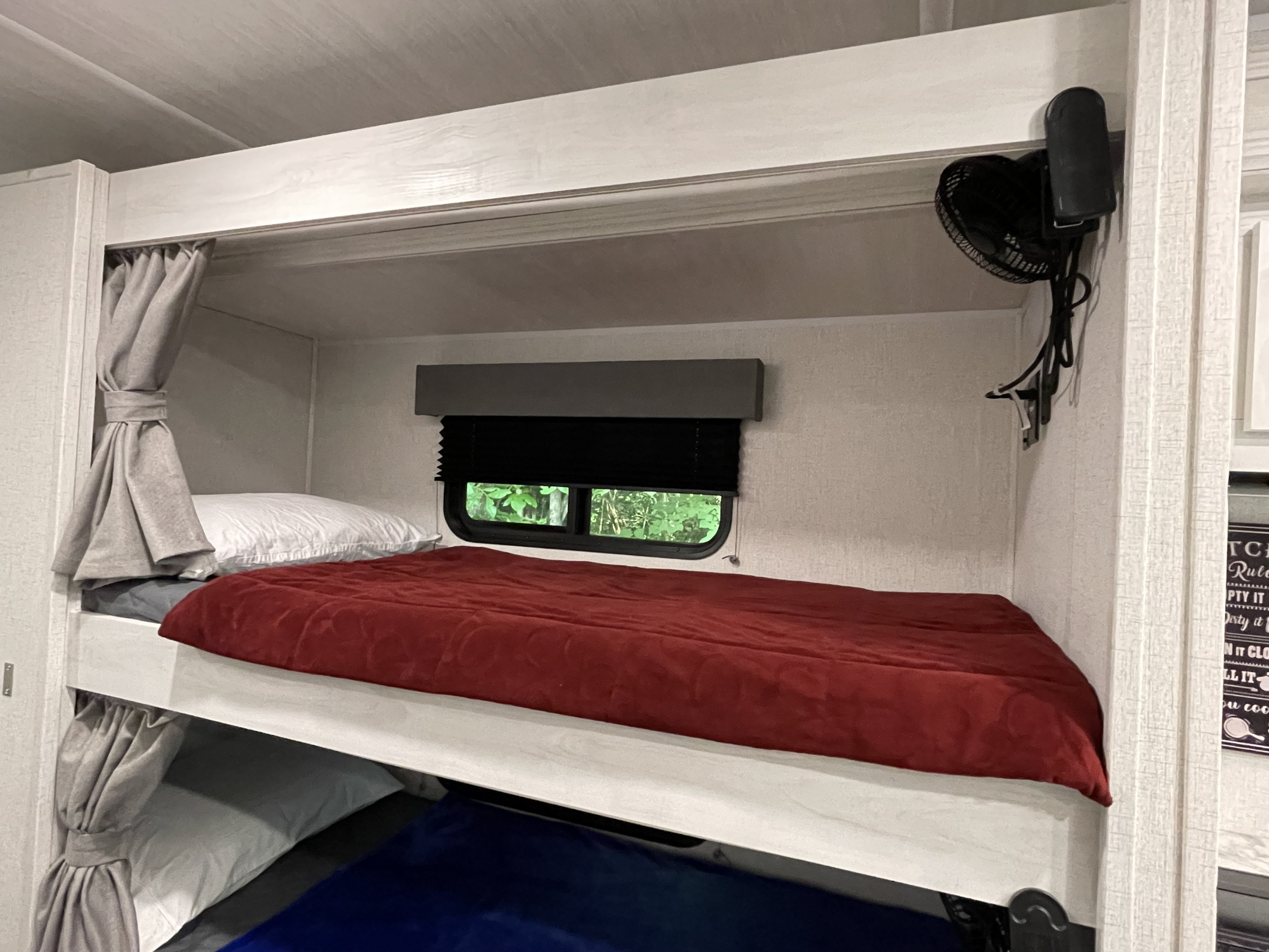 Comfortable bunk beds in this RV rental, with a red comforter, window, and fan for a cozy camper interior.. East to West Entrada 3100FB 2022