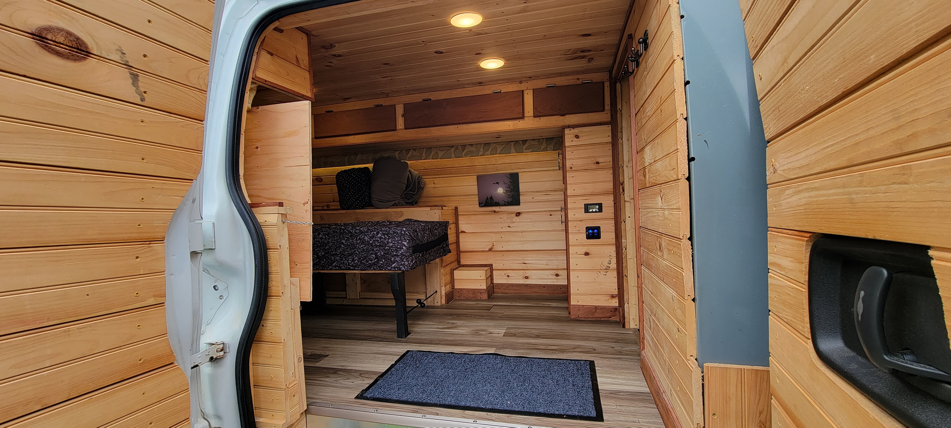 Step inside this custom wood-paneled RV rental, showcasing a compact interior with a bed, storage, and controls.. GMC Savanna 2014