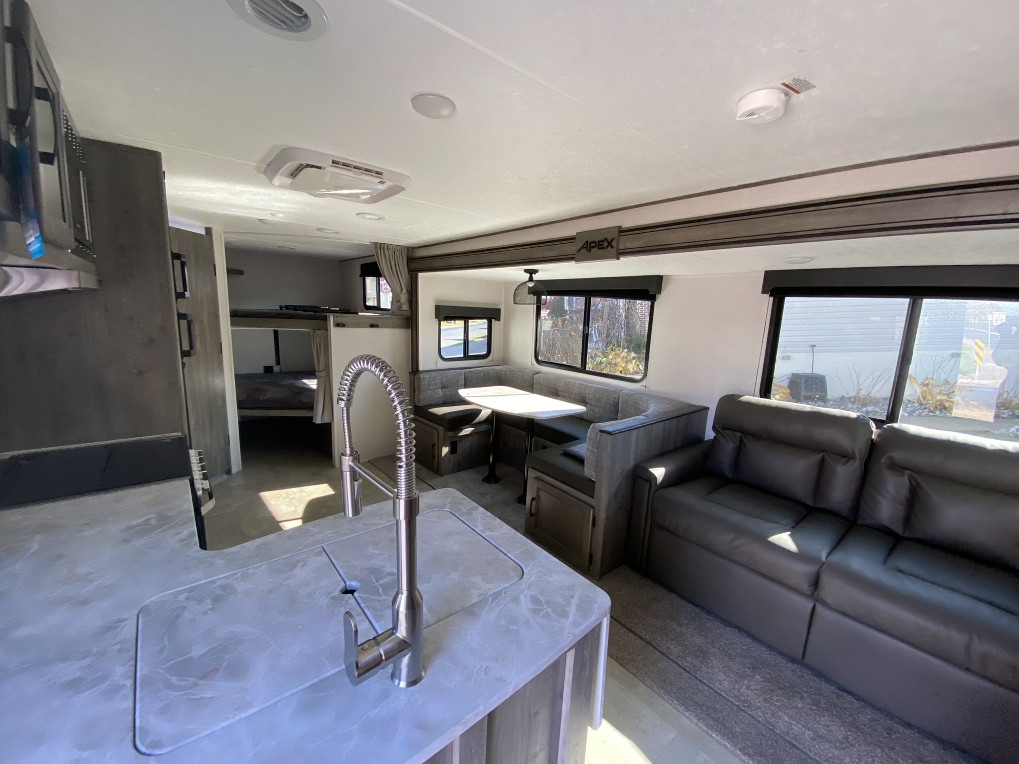 RV rental interior features a kitchen with sink, dinette, comfy sofa, and bunk beds. Spacious and ready for adventure!. Coachmen Apex 2021
