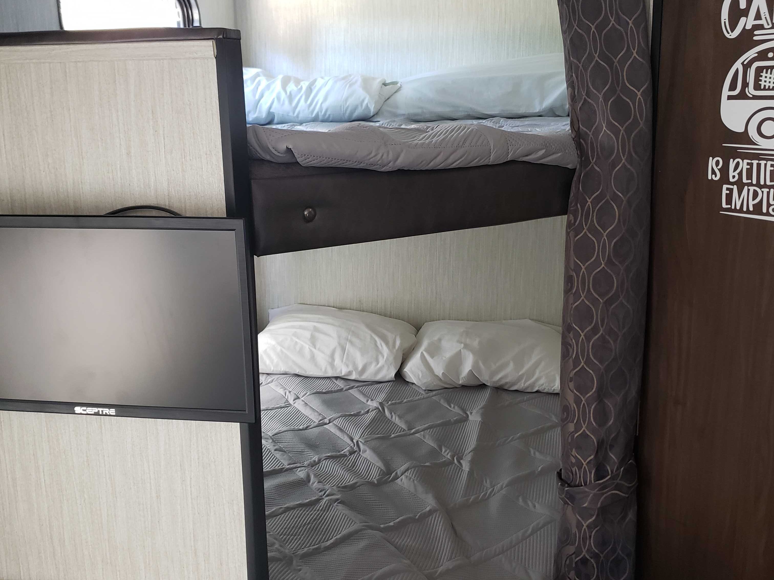 RV rental interior: Bunk beds with crisp bedding and a SCEPTRE TV. A patterned curtain adds privacy. Compact and functional.. Forest River Cherokee Grey Wolf Special Edition 2020