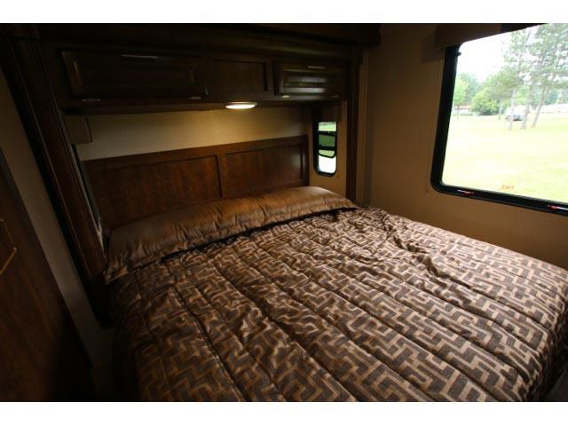 This RV rental bedroom offers a cozy bed with patterned bedding, wood cabinets, and a window for scenic views.. Forest River FR3 30DS 2014