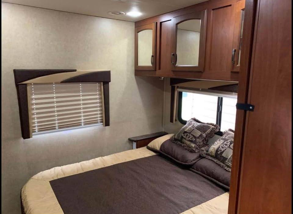 This RV rental bedroom features a comfortable bed, overhead cabinets with mirrors, and window blinds. Cozy, functional design.. Jayco Greyhawk 2014