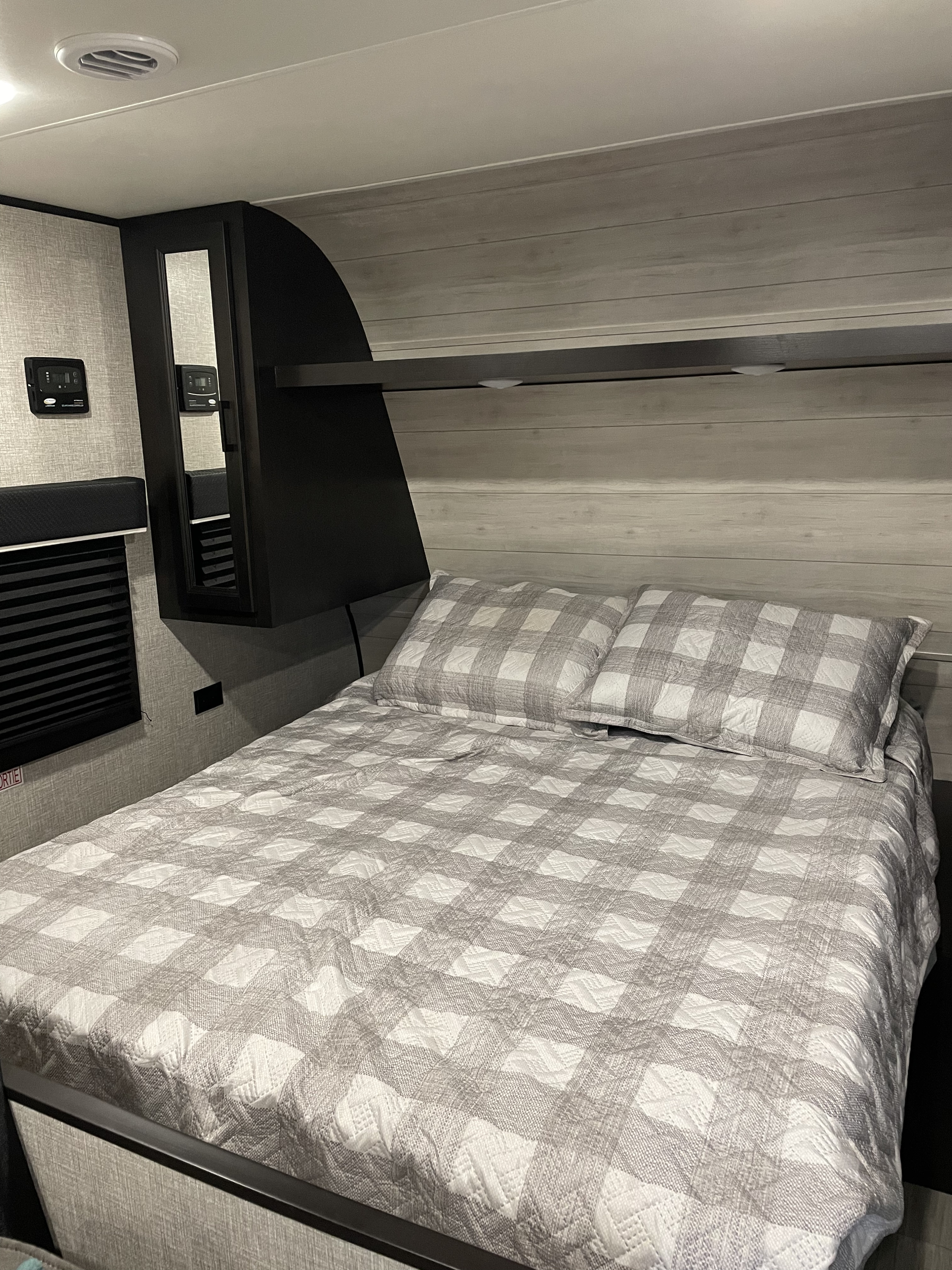 Cozy RV rental bedroom featuring a grey plaid bed, overhead storage, wall controls, and ceiling vent.. Jayco Jay Flight 2022