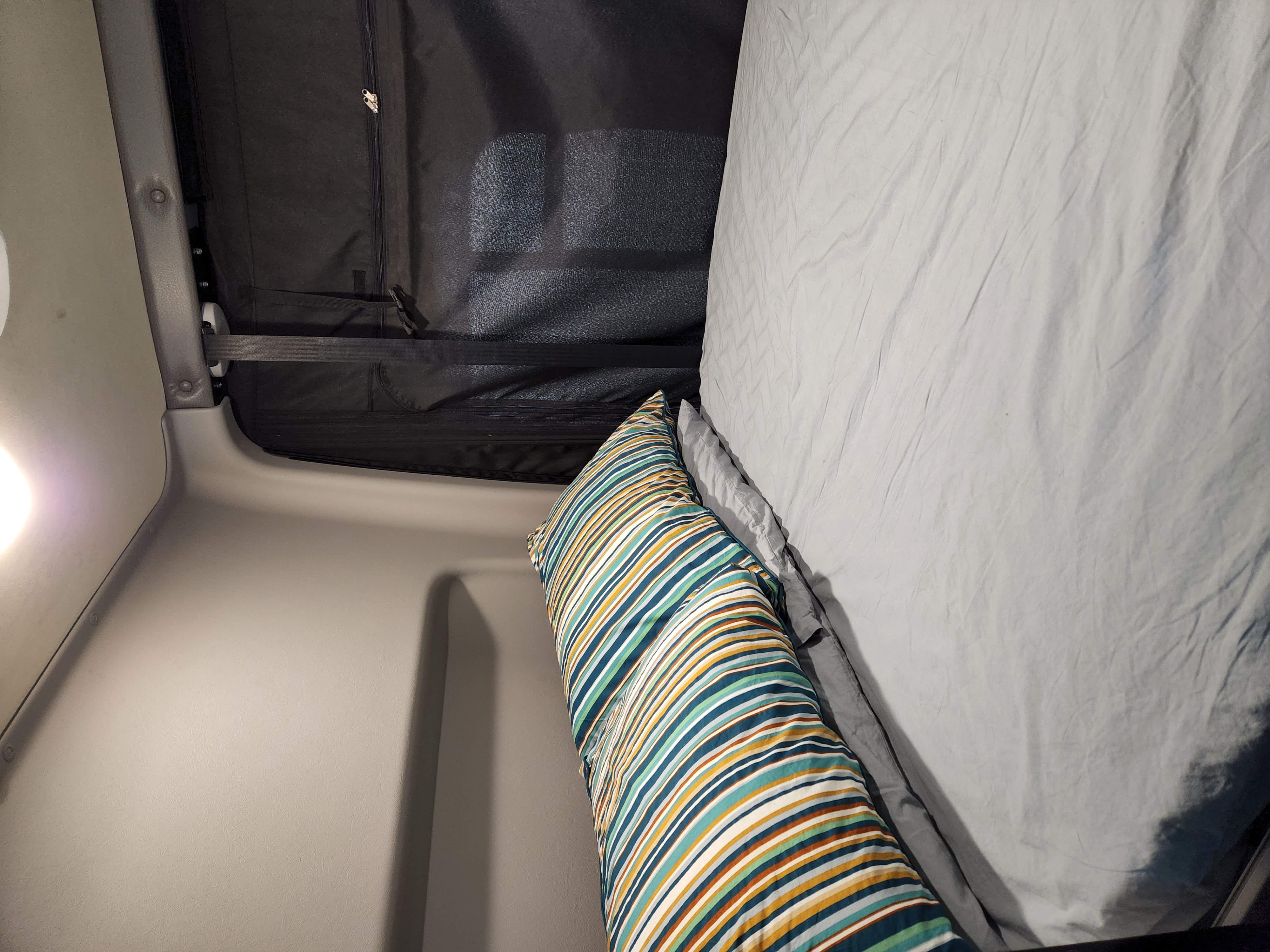 Cozy RV rental camper bed with a striped pillow and dark window cover, perfect for a restful sleep on the road.. Winnebago Revel 2022