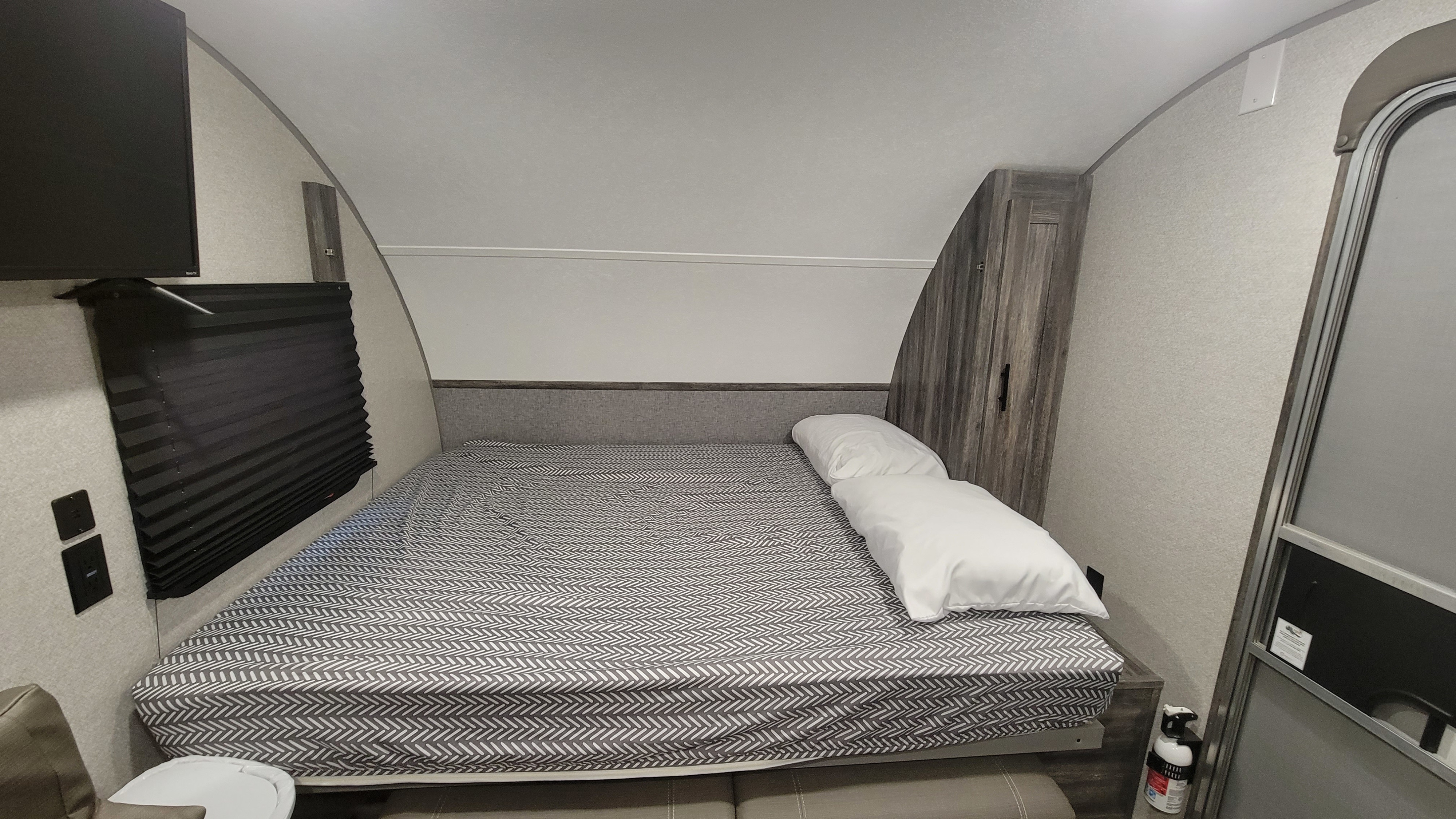 Cozy RV rental bedroom featuring a patterned bed, TV, window, and cabinet. Fire extinguisher visible by the door.. Forest River Wildwood FSX Platinum 2020