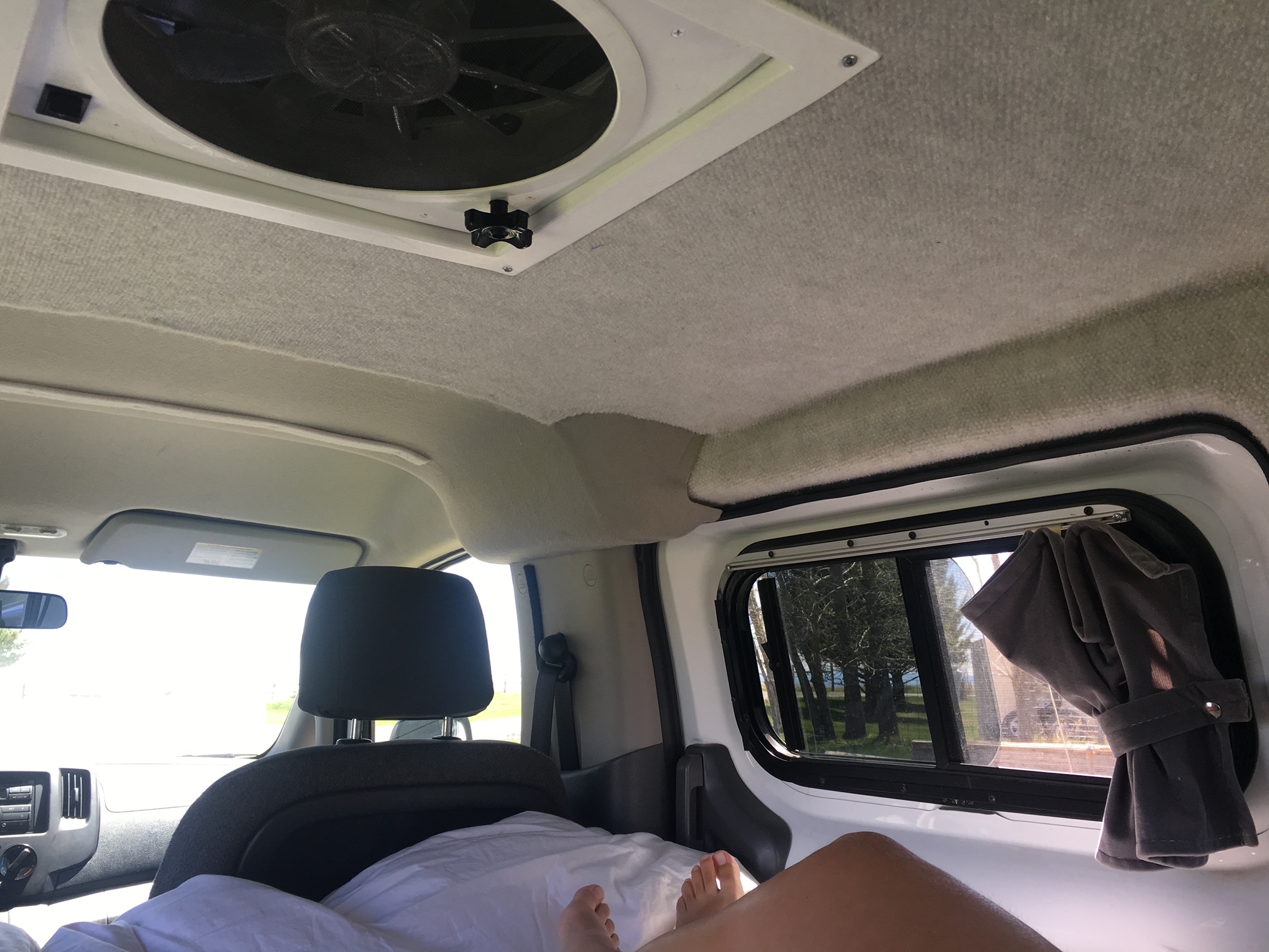 Comfortable rv rental interior with a ceiling fan, bed (feet visible), and a scenic side window view. Great for van life.. Nissan PRIMASTAR 2014