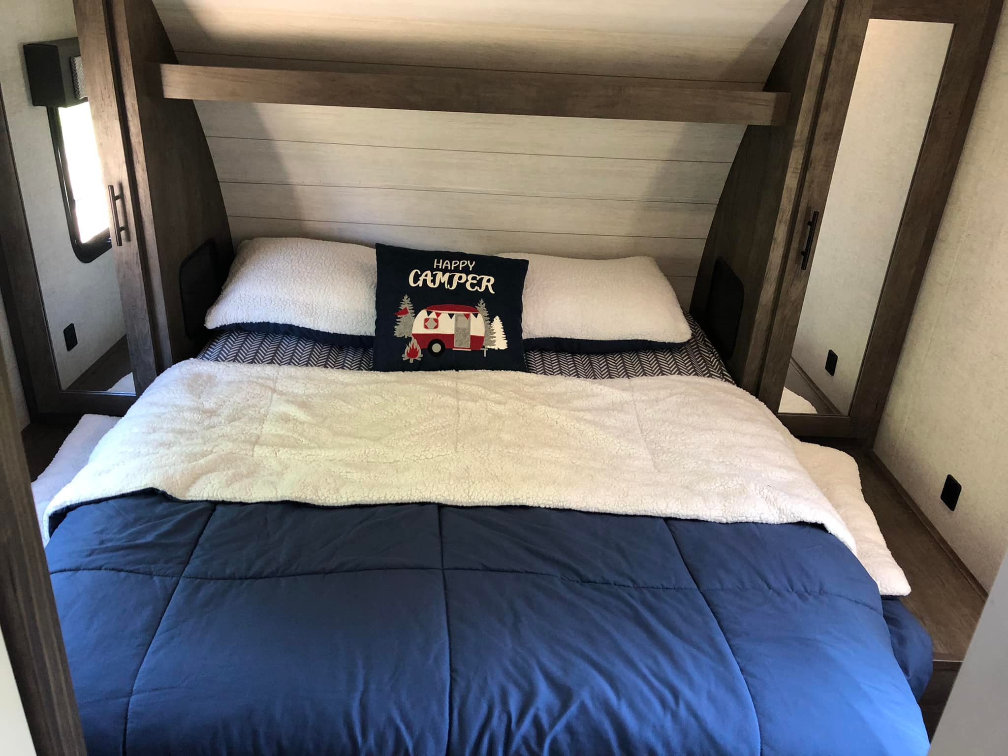 Cozy RV rental bedroom featuring a comfy bed with a blue comforter, fluffy white blanket, and "Happy Camper" pillow.. Forest River Salem Cruise Lite 2020
