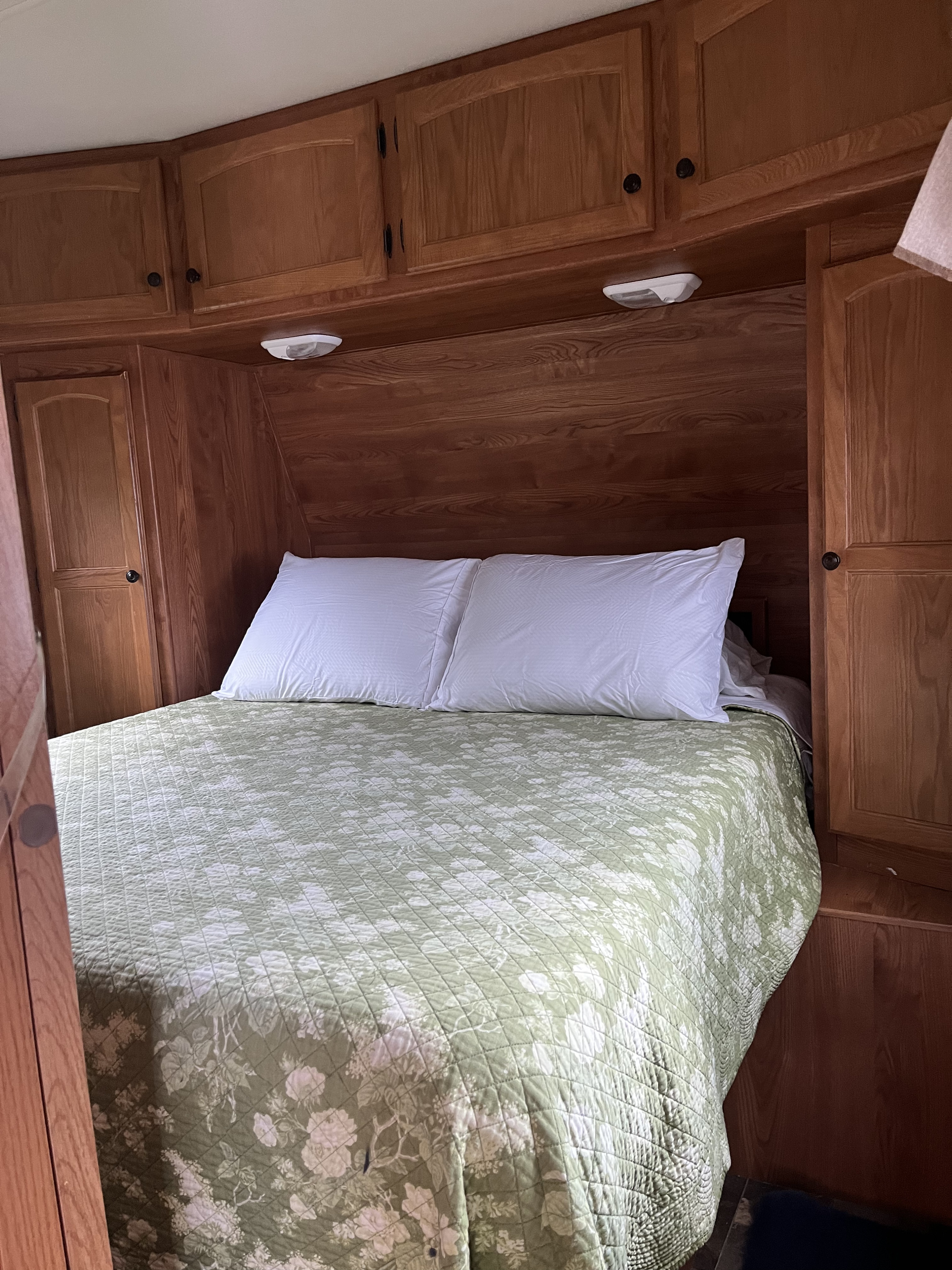 RV rental bedroom: a cozy space with a bed, green floral quilt, white pillows, and integrated wooden cabinets.. Heartland RVs North Country SLT 2012