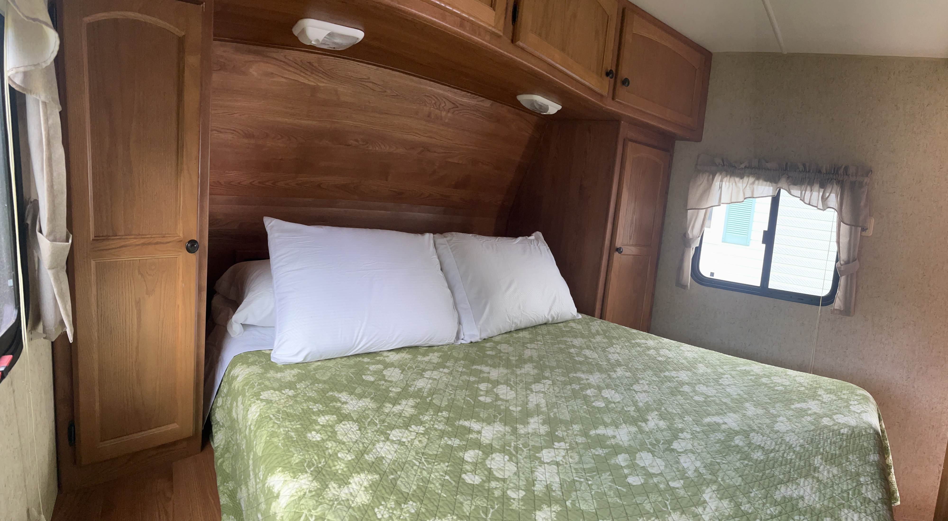 Cozy RV rental bedroom with a comfy bed, green floral quilt, wooden cabinets, and window, perfect for your next trip.. Heartland RVs North Country SLT 2012
