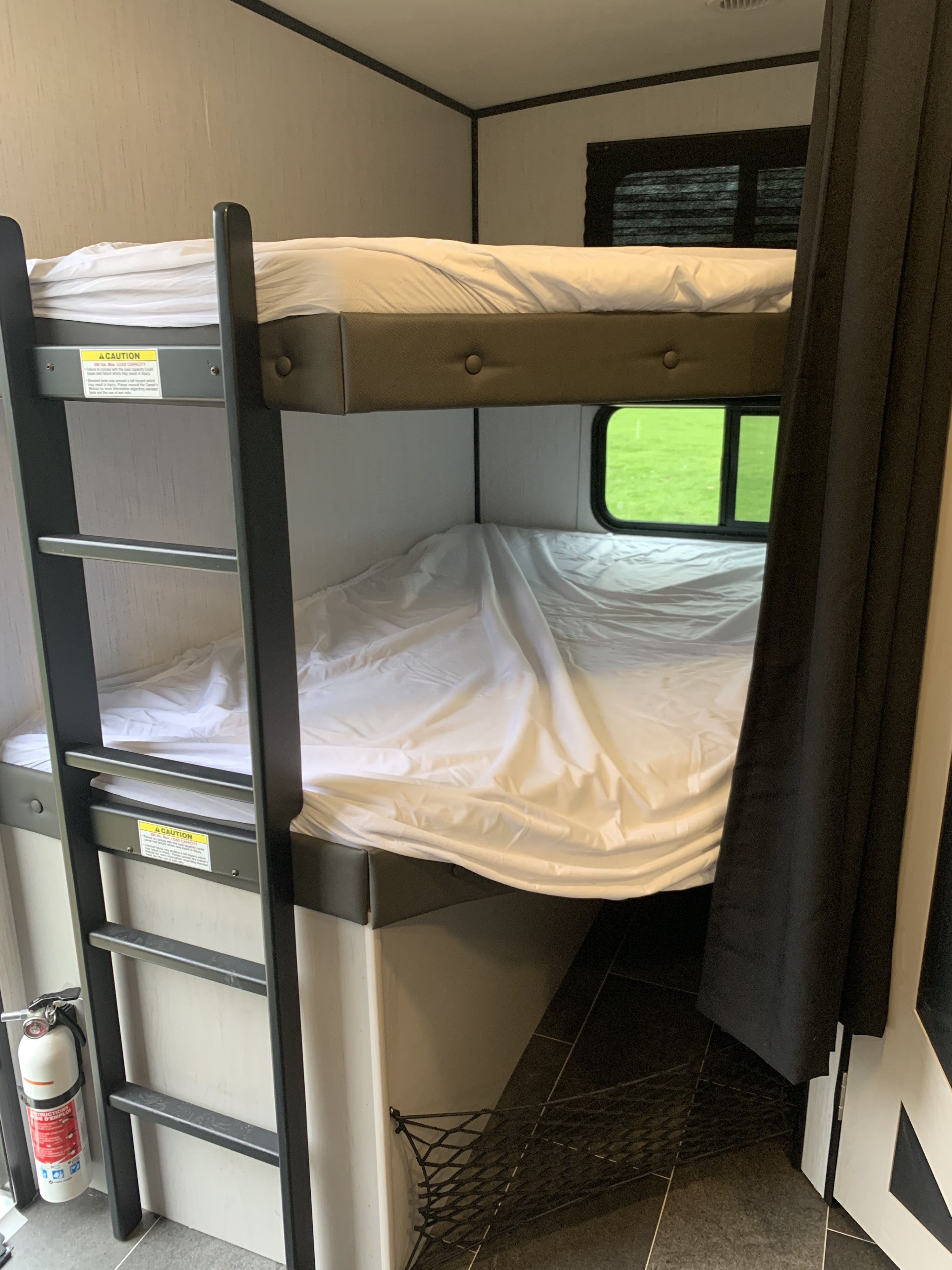 A functional RV rental interior featuring comfortable bunk beds with a ladder, window, and essential fire safety gear.. Heartland RVs Mallard 2022