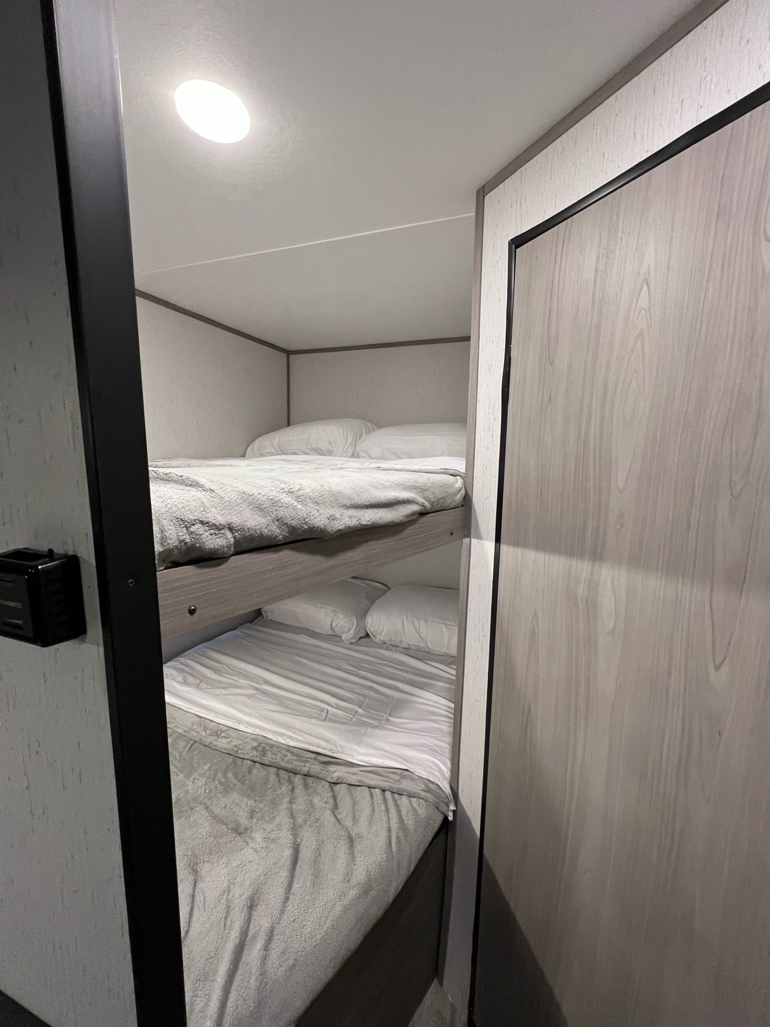 Clean bunk beds in a modern rv rental, offering compact sleeping space with white bedding and light gray walls.. Dutchmen Coleman Lantern LT 2022