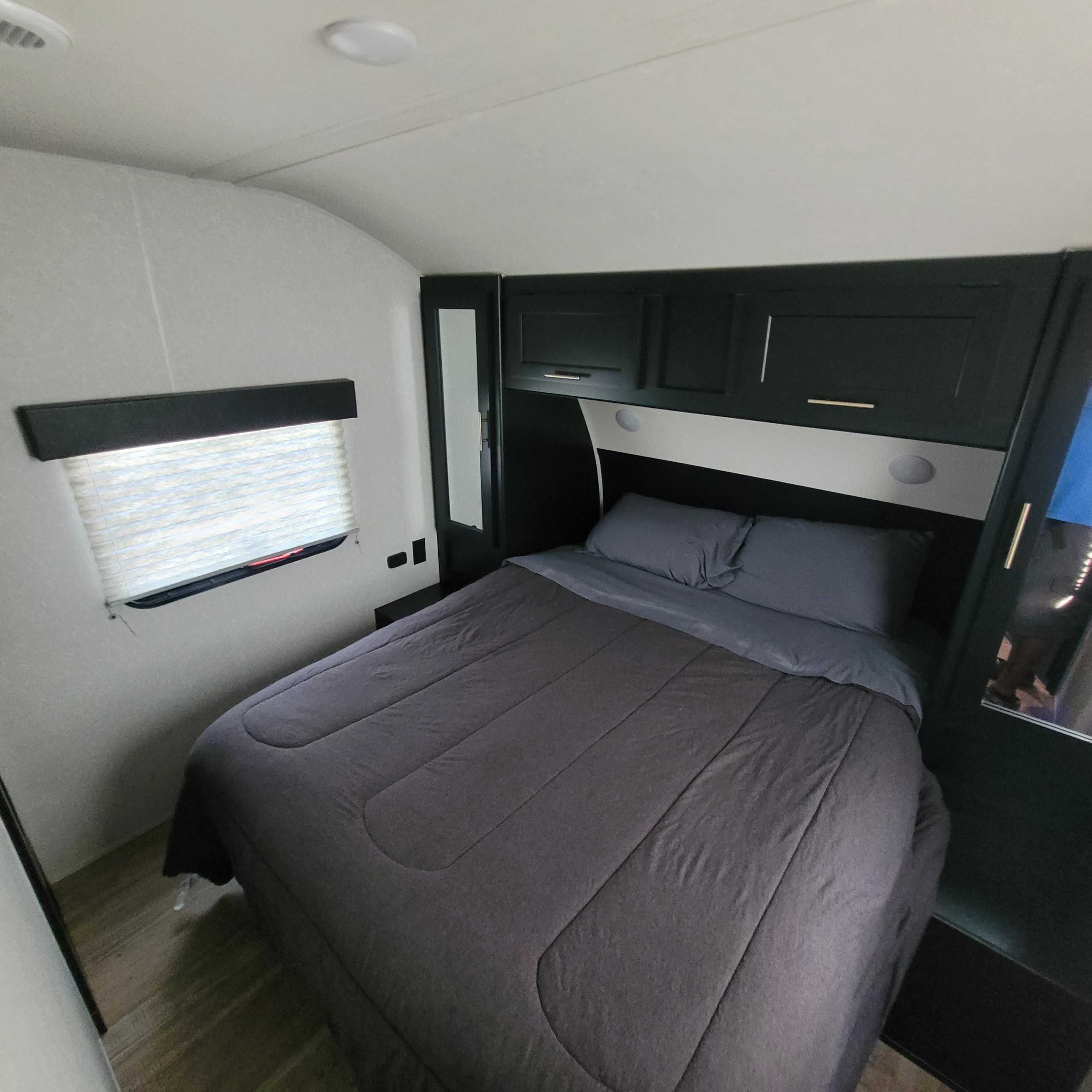 Inside this **RV rental** bedroom: a comfy bed with dark bedding, modern built-in storage, and a window. Ideal for road trips!. Forest River Cherokee 2022