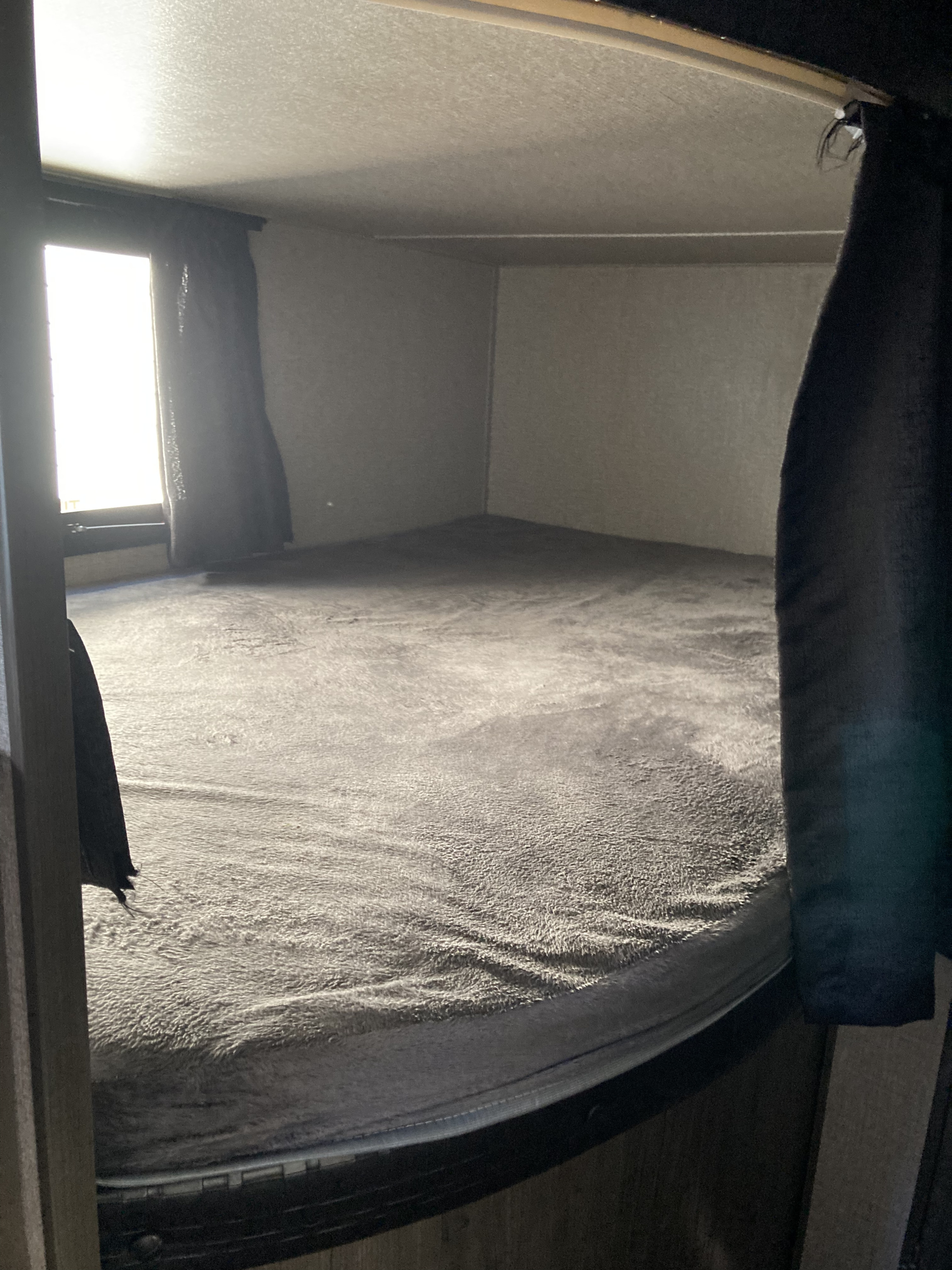 Cozy RV rental bunk bed with plush grey bedding by a bright window, offering a comfortable sleeping space.. Jayco Jay Flight SLX 2021