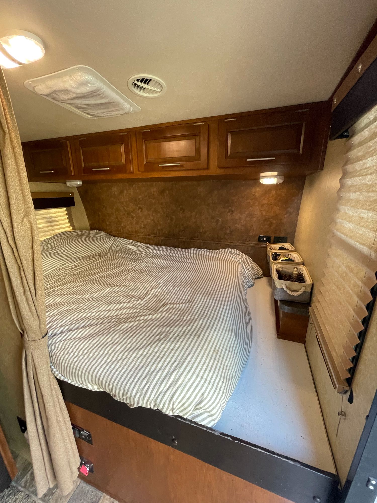 Cozy RV rental bedroom featuring striped bedding, wooden overhead cabinets, and compact storage. Good lighting and ventilation.. Forest River X-Lite 2015