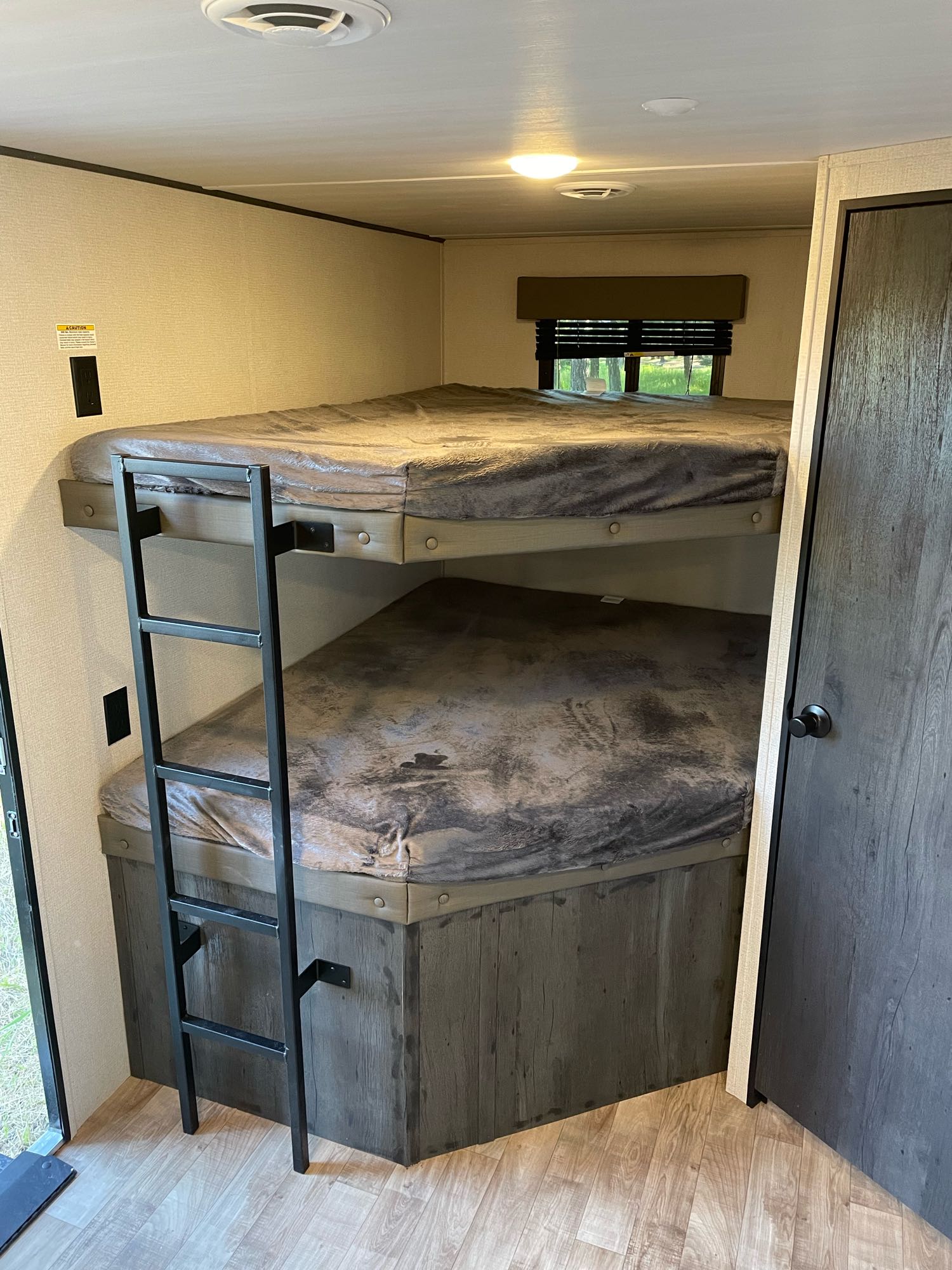 Inside an RV rental: dark grey bunk beds with a ladder, wood flooring, and a window for sleeping.. Keystone RV Hideout 2022