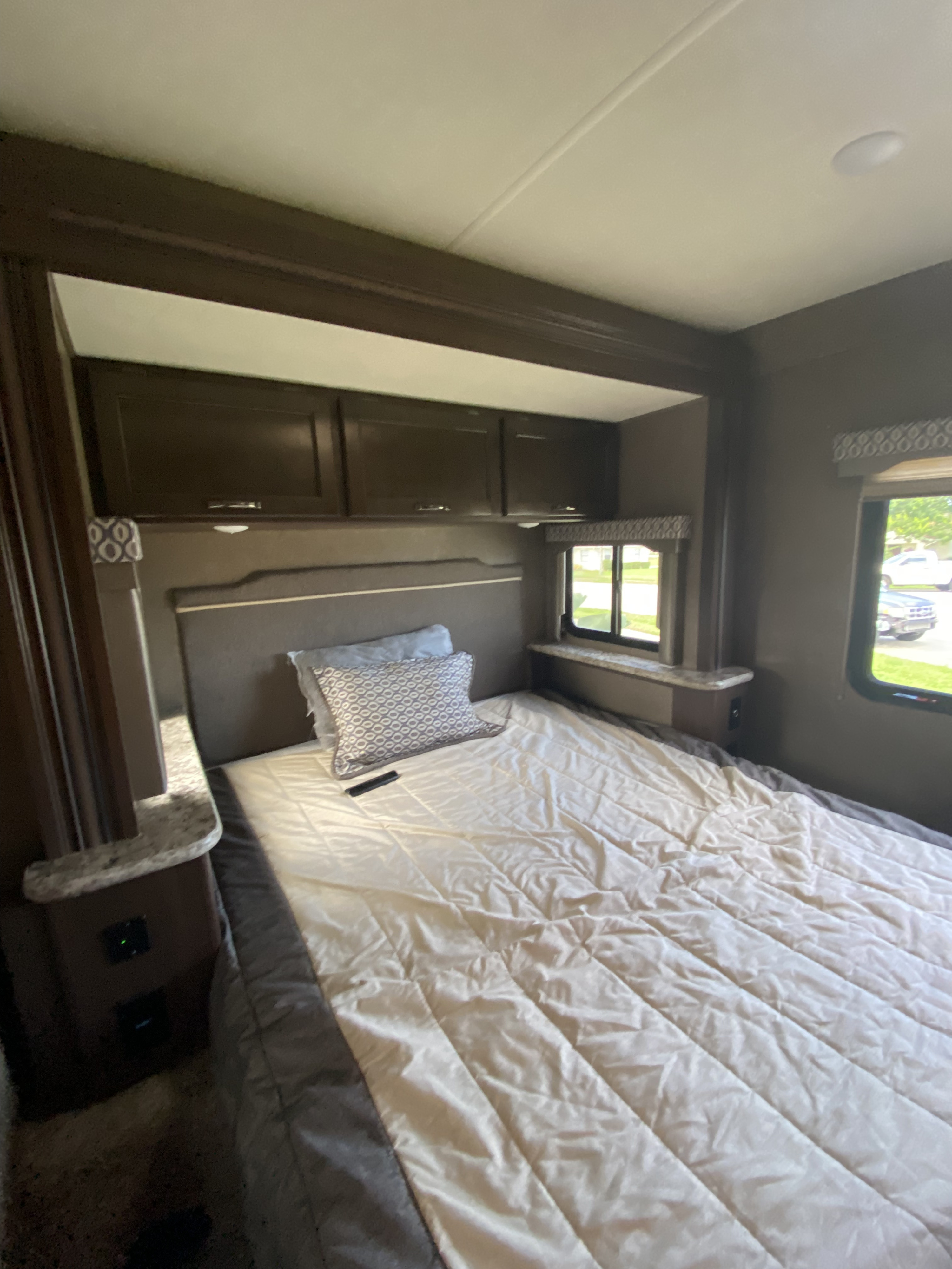 Comfortable RV rental bedroom with overhead cabinets, a cozy bed, and natural light from wide windows, perfect for travel.. Thor Freedom Elite 2019