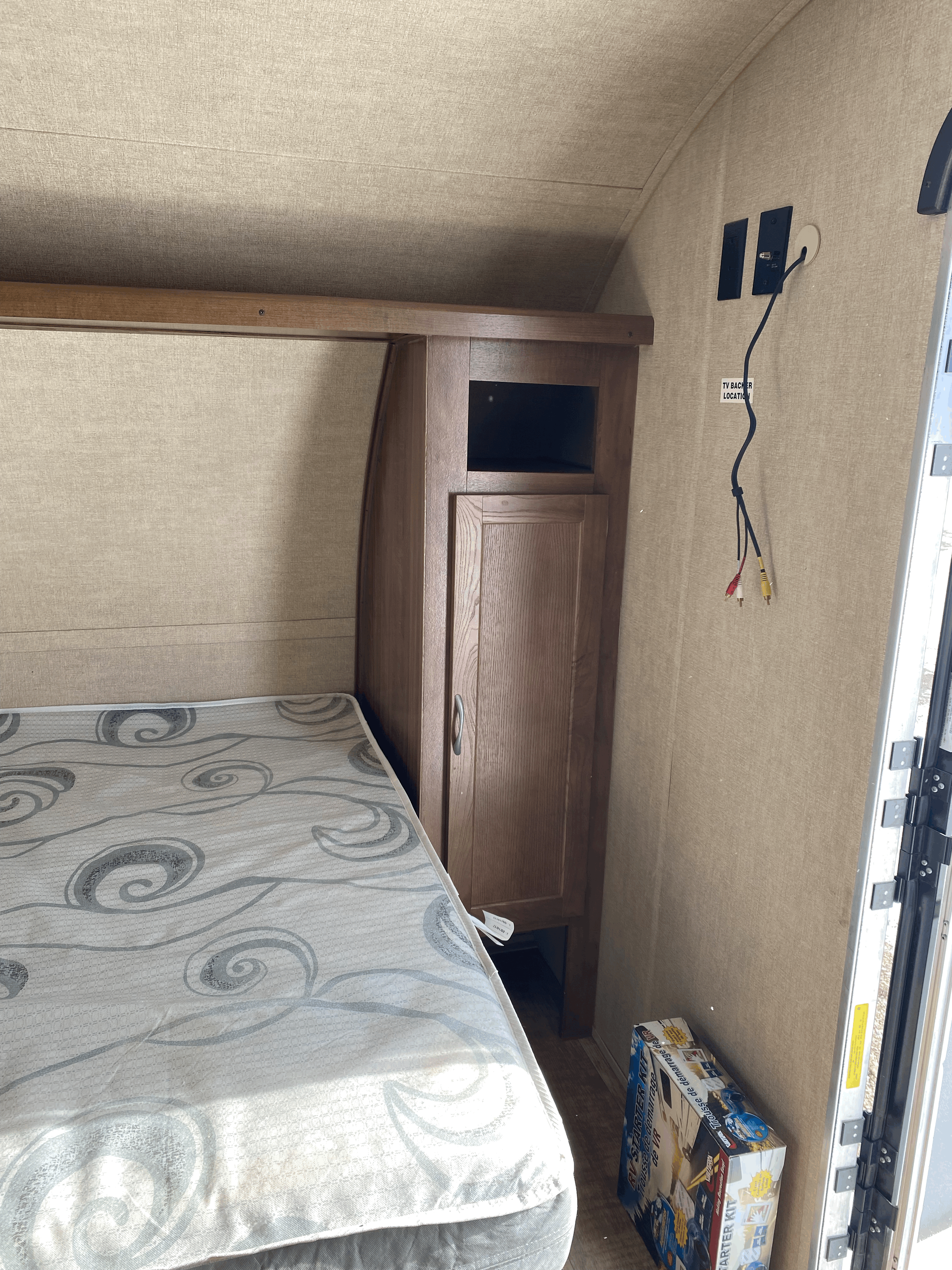 RV rental bedroom with bed, built-in storage, TV hookups, and an RV starter kit box, showing cozy interior setup.. Gulf Stream Kingsport Super Lite 2018