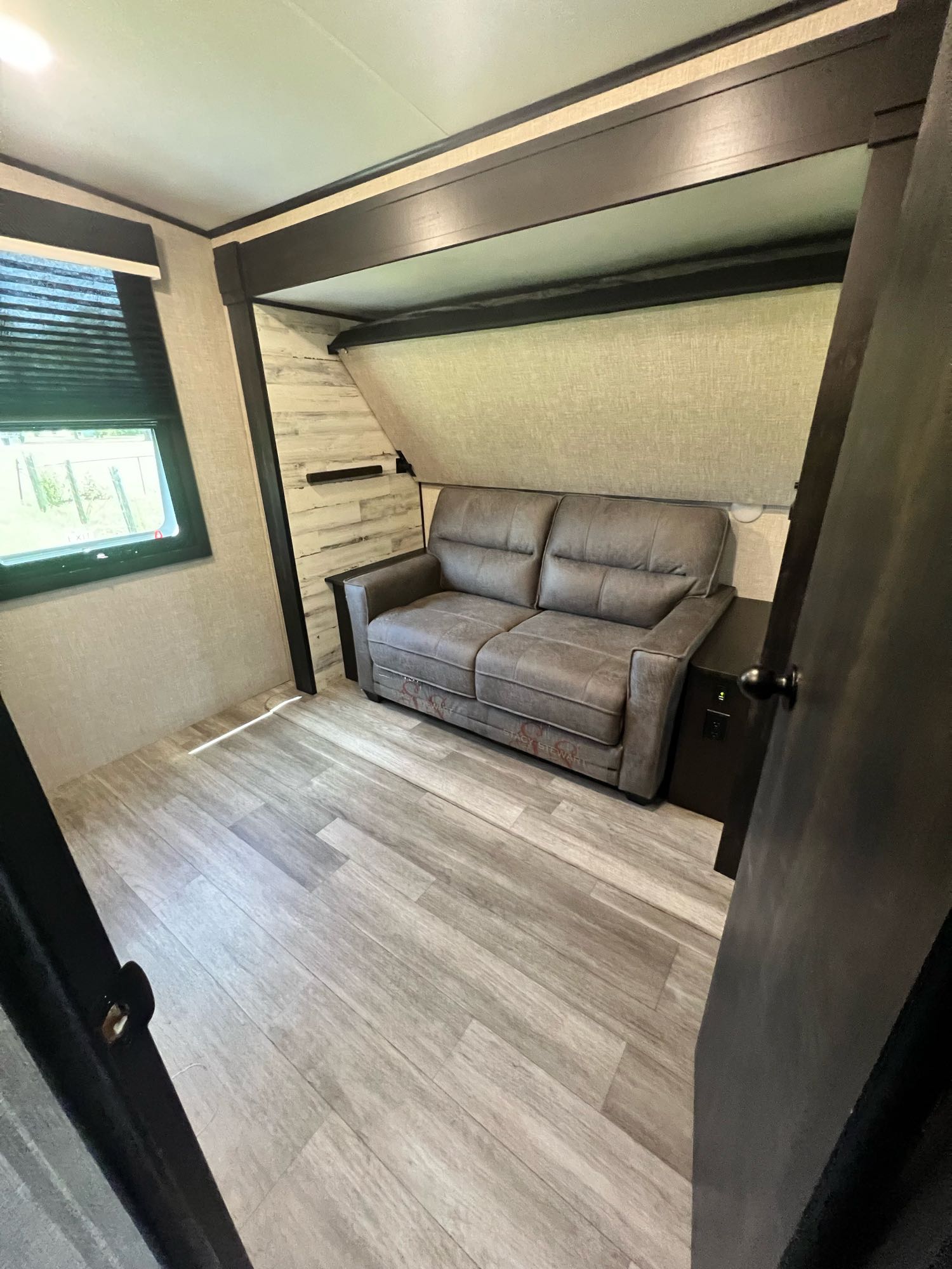 This RV rental's versatile living space features a gray sofa, wood-look floor, and an overhead bunk or storage area.. Jayco White Hawk 2022