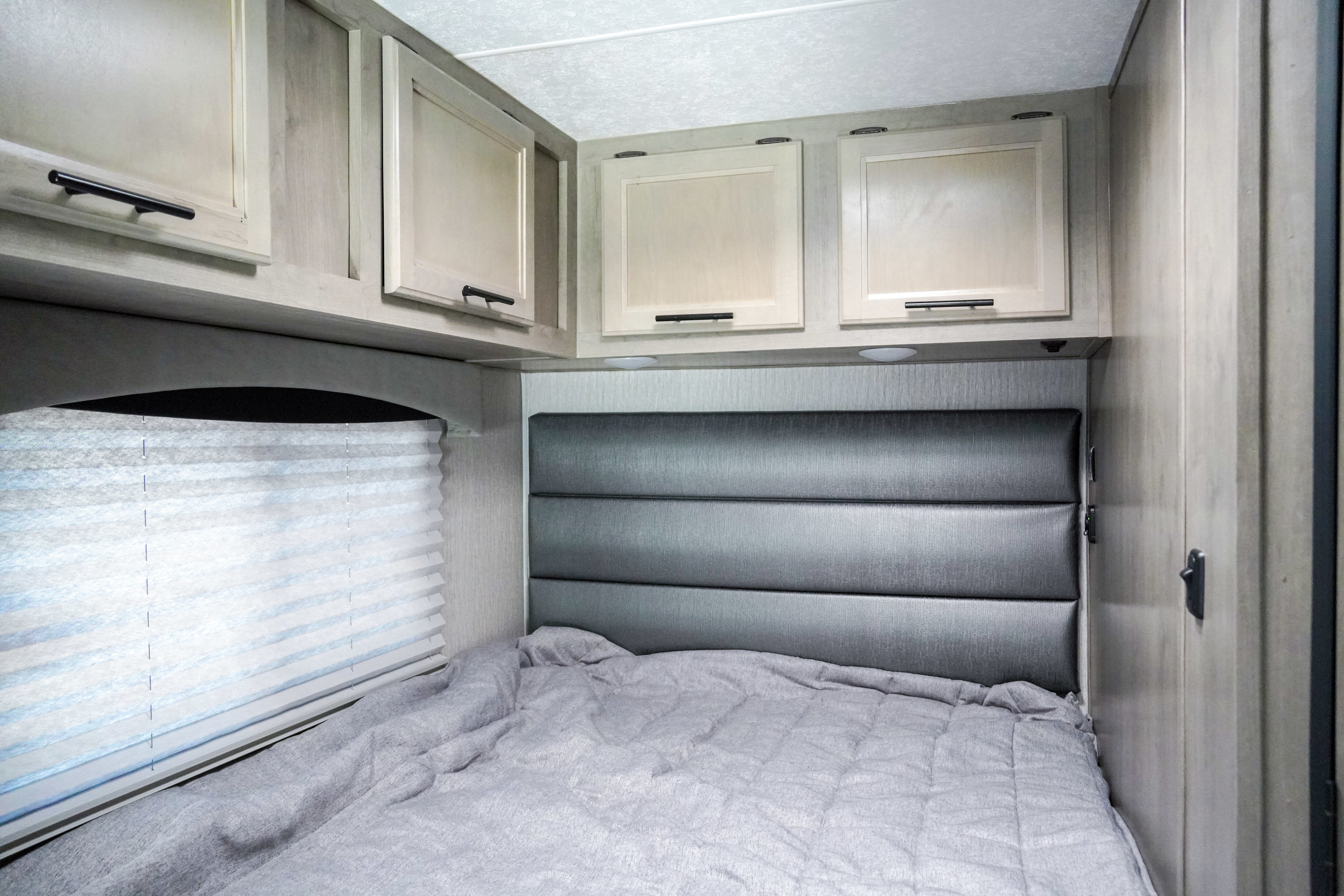 Inside an RV rental, a well-lit bedroom features a comfy bed, padded headboard, and storage cabinets.. Forest River Coachmen Cross Trail XL 2022