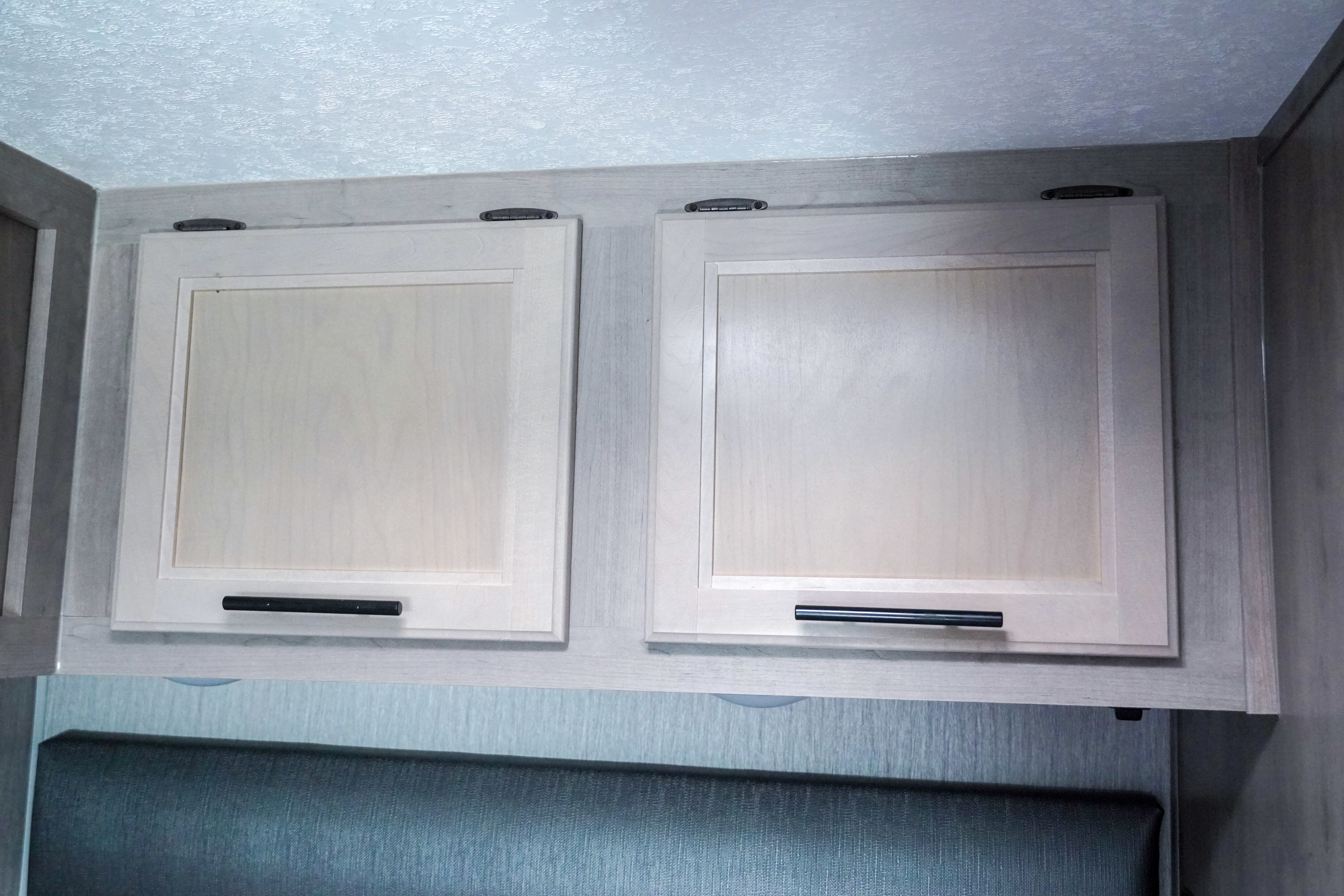 RV rental light wood overhead cabinets with black handles, offering convenient storage above a bedroom headboard.. Forest River Coachmen Cross Trail XL 2022