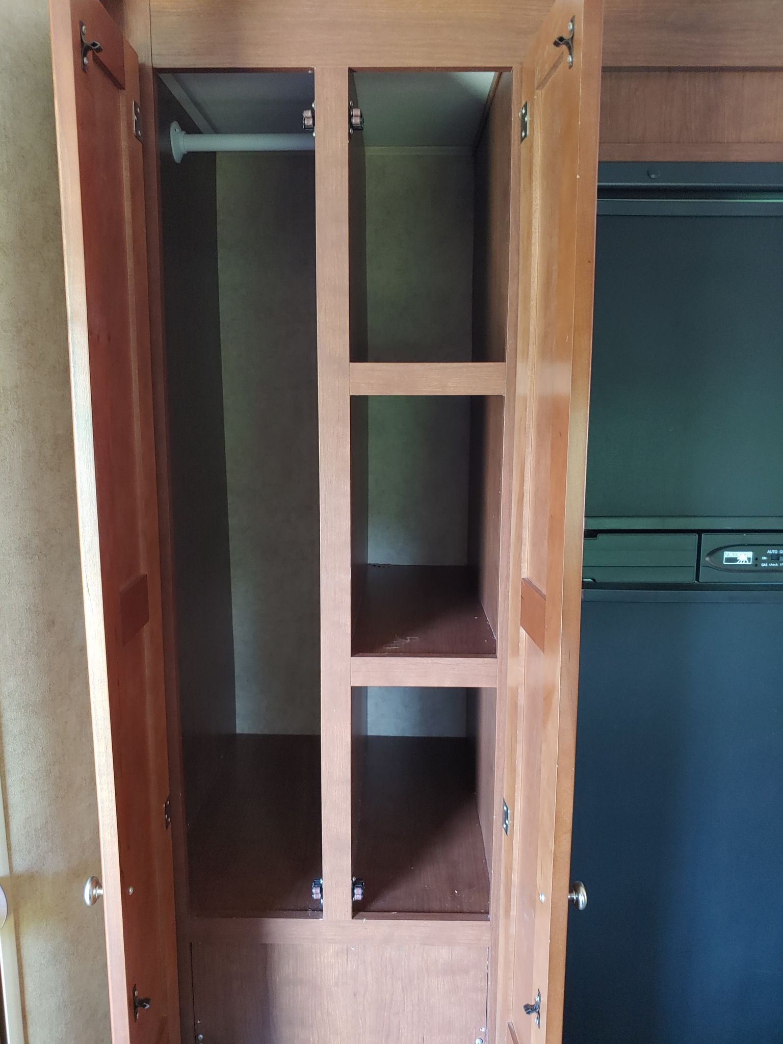 RV rental: Open wooden wardrobe with a hanging rod and shelves, offering interior storage next to a refrigerator.. Dutchmen Kodiak 2012