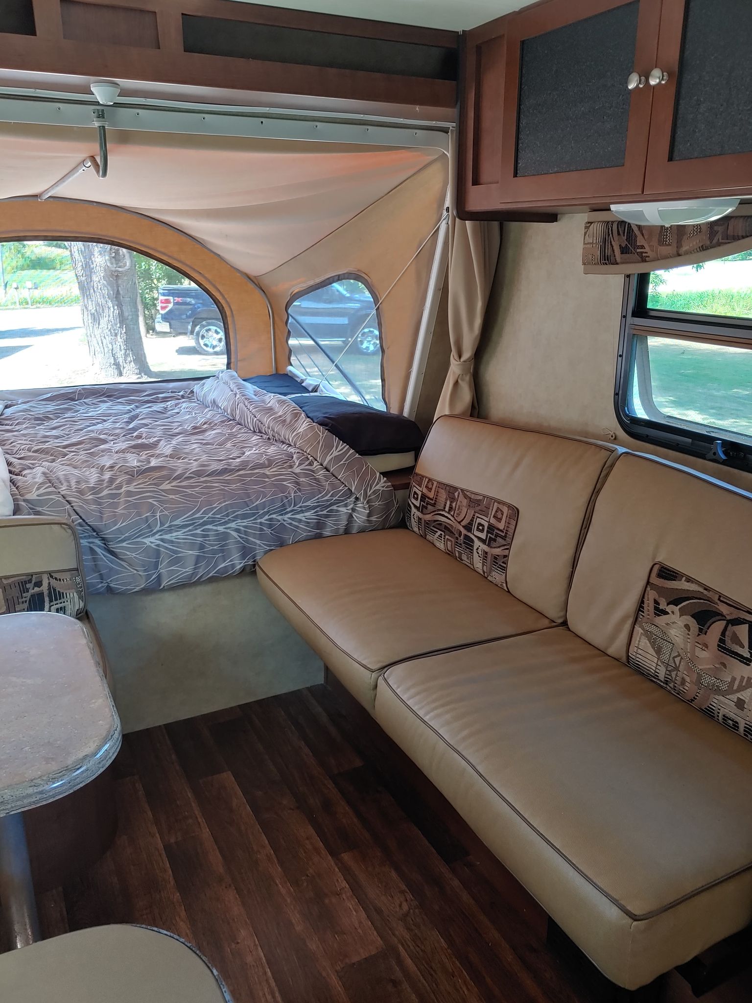 RV rental interior view: large bed with grey comforter, tan sofa, and wood flooring. Enjoy comfortable camping trips!. Dutchmen Kodiak 2012