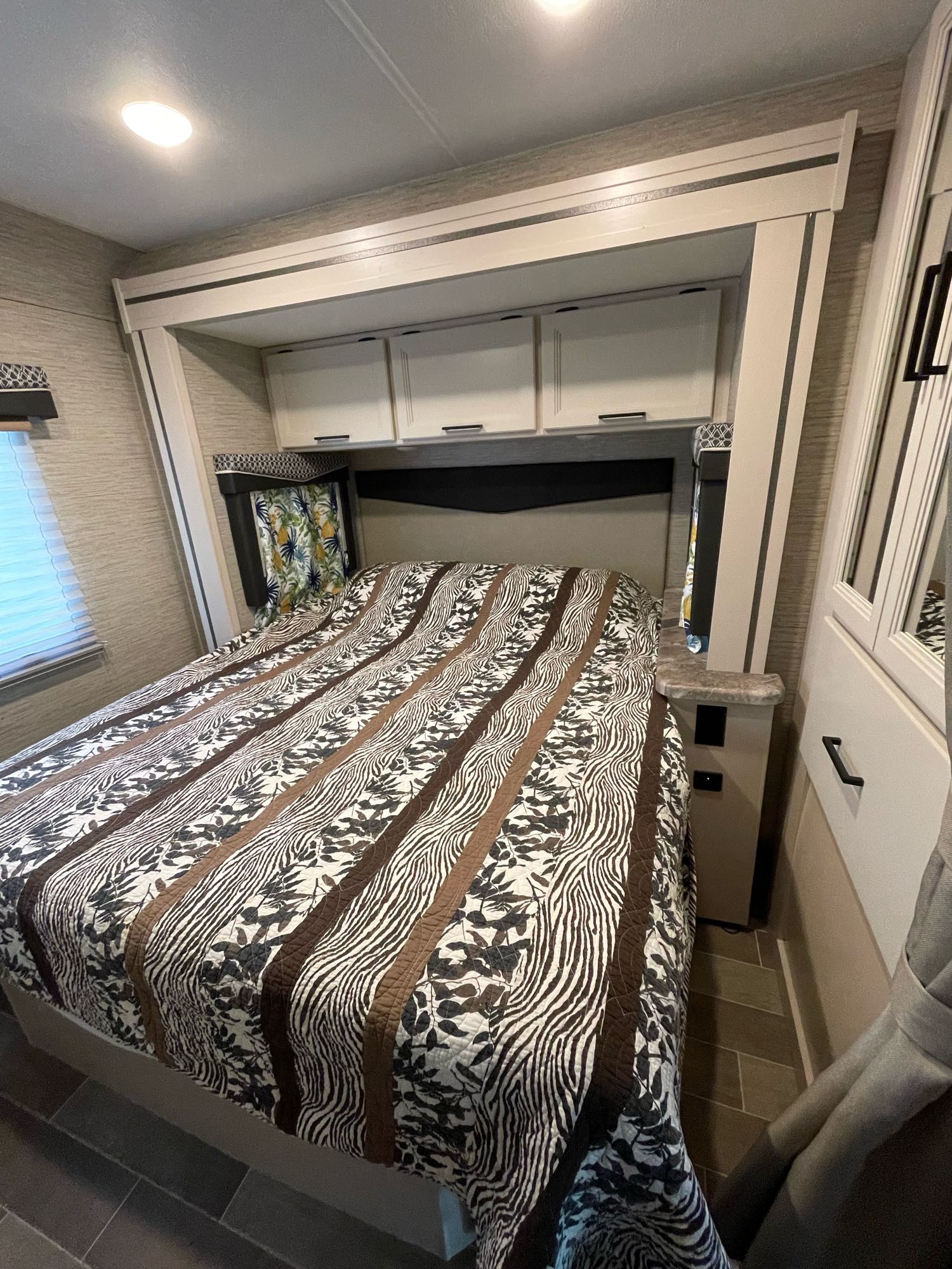 Cozy RV rental bedroom with patterned bed, overhead storage, and window, perfect for travel comfort.. Thor Chateau 2022
