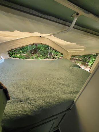 RV rental interior: A comfortable bed with a green quilt inside a pop-up camper, offering refreshing forest views.. Forest River Rockwood Roo 2000