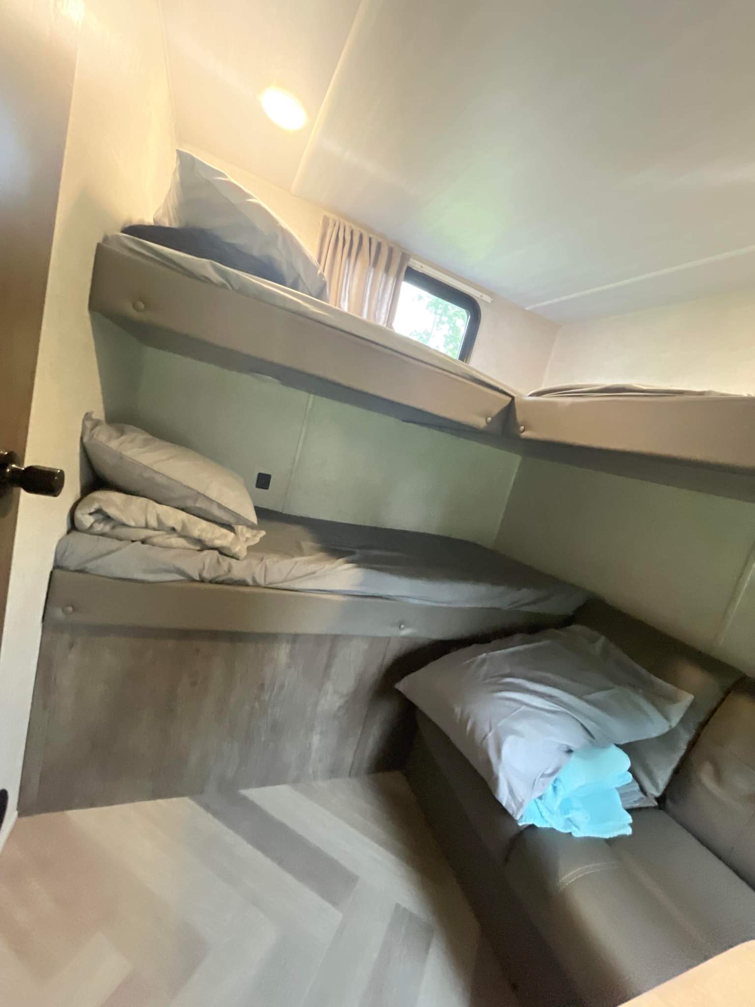 Compact RV rental interior featuring stacked bunk beds, a small window, and a lounge sofa with light bedding.. wildwood x-lite 273qxlb 2021