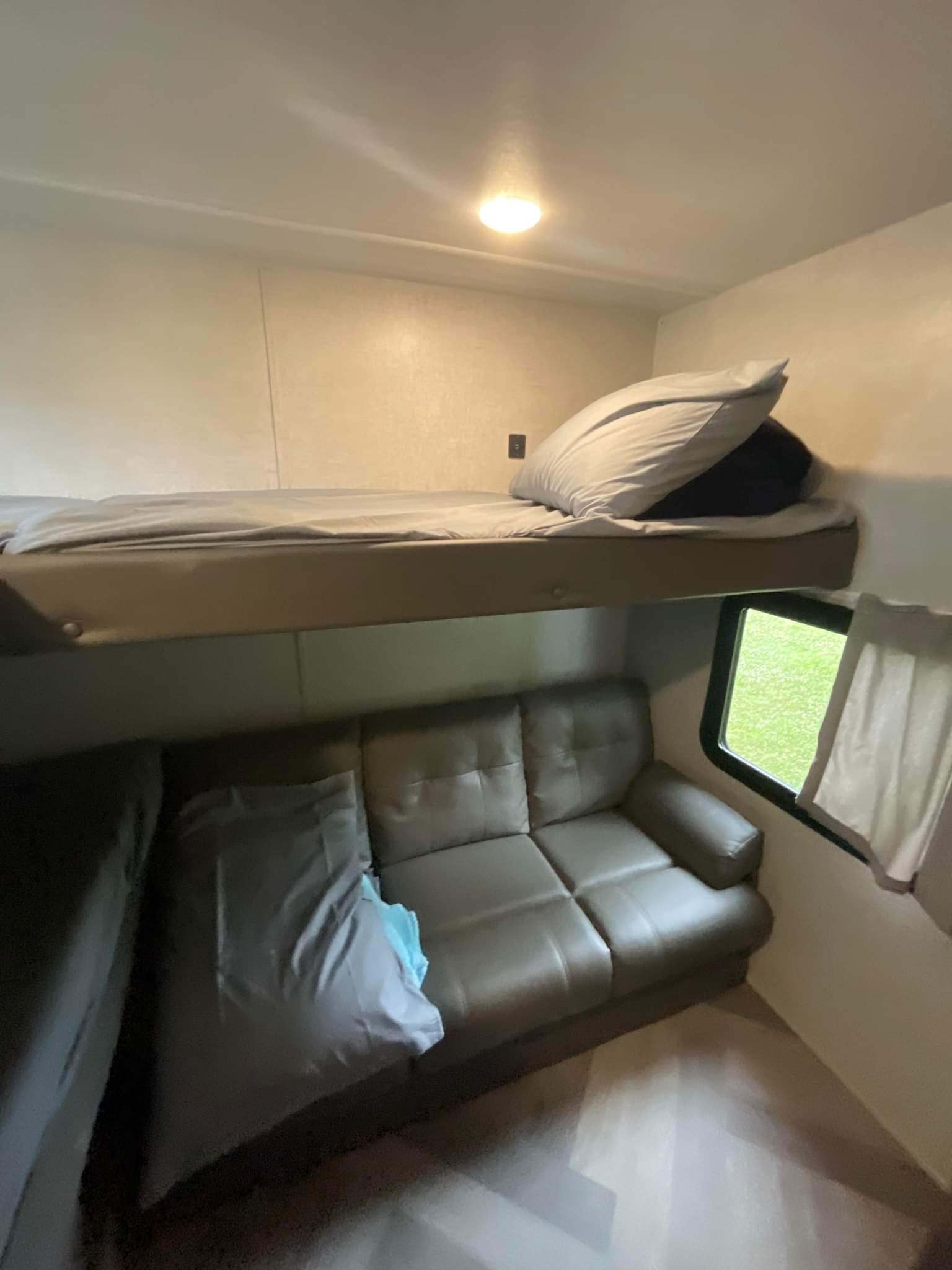 Comfortable RV rental interior: bunk bed, gray sofa, and window overlooking green space. Ready for your trip!. wildwood x-lite 273qxlb 2021