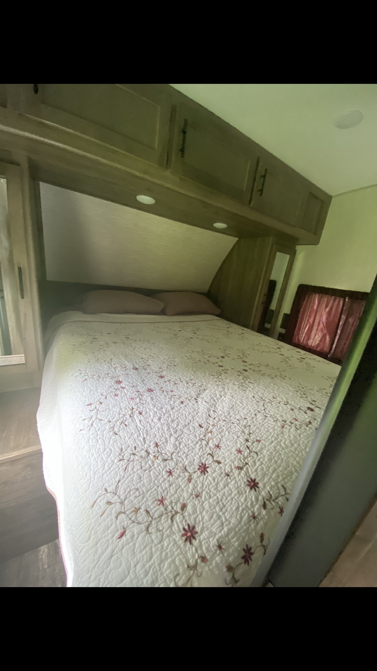 Cozy RV rental bedroom with a white floral quilted bed, two pink pillows, and built-in wooden storage cabinets.. Forest River Cherokee Wolf Pack Toy Hauler 2020