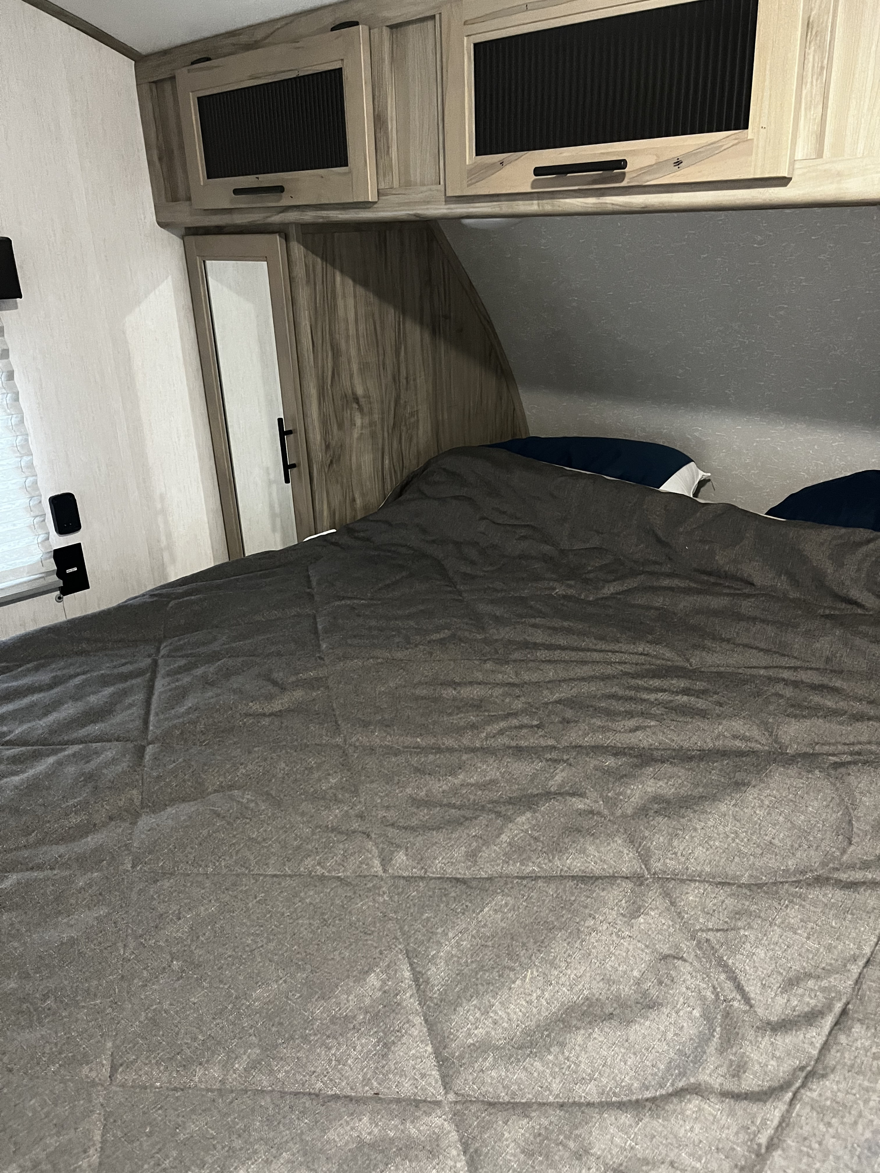 This RV rental bedroom features a dark grey comforter on the bed, overhead cabinets, and a mirror-fronted wardrobe.. Forest River Cherokee Alpha Wolf 2021