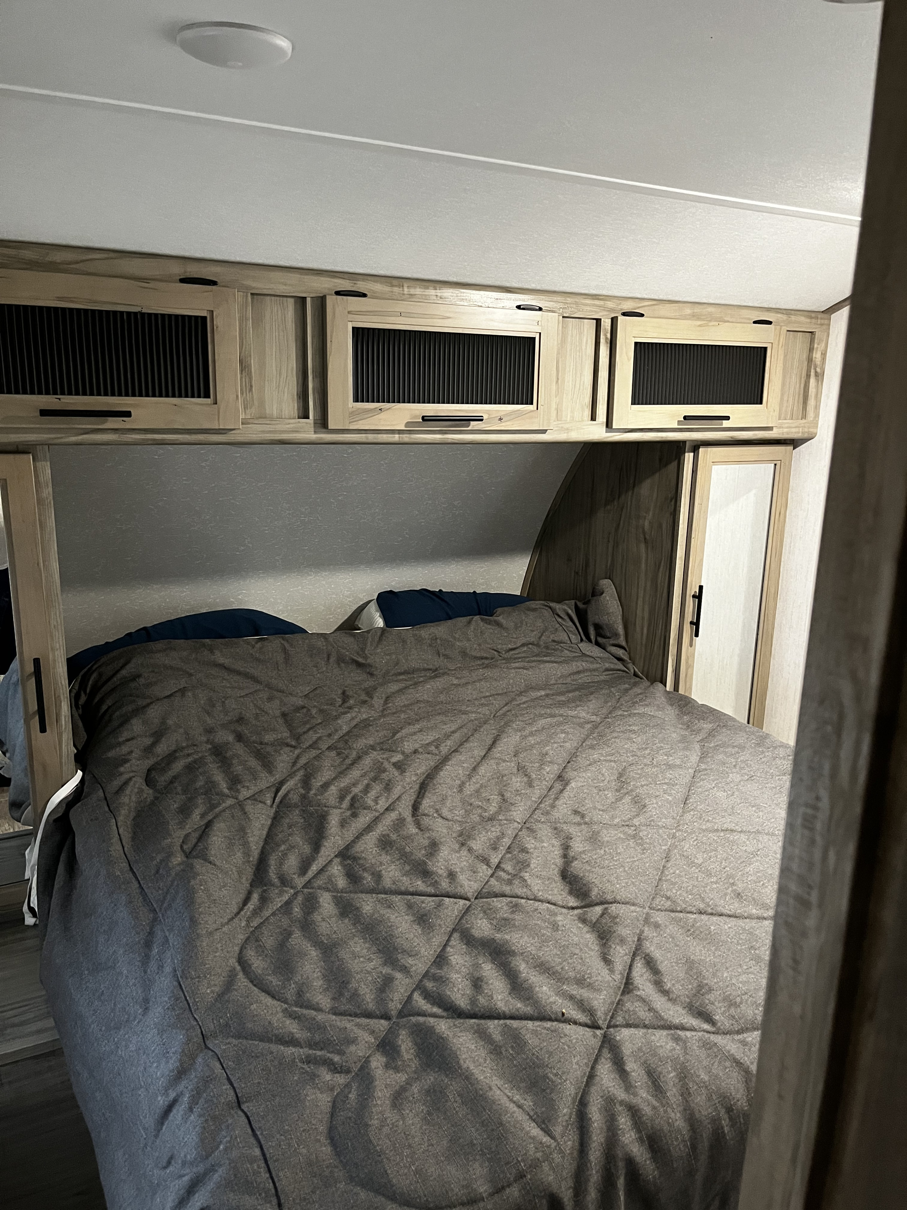 Cozy RV rental bedroom featuring a comfortable bed with a gray comforter, overhead storage cabinets, and ceiling light.. Forest River Cherokee Alpha Wolf 2021