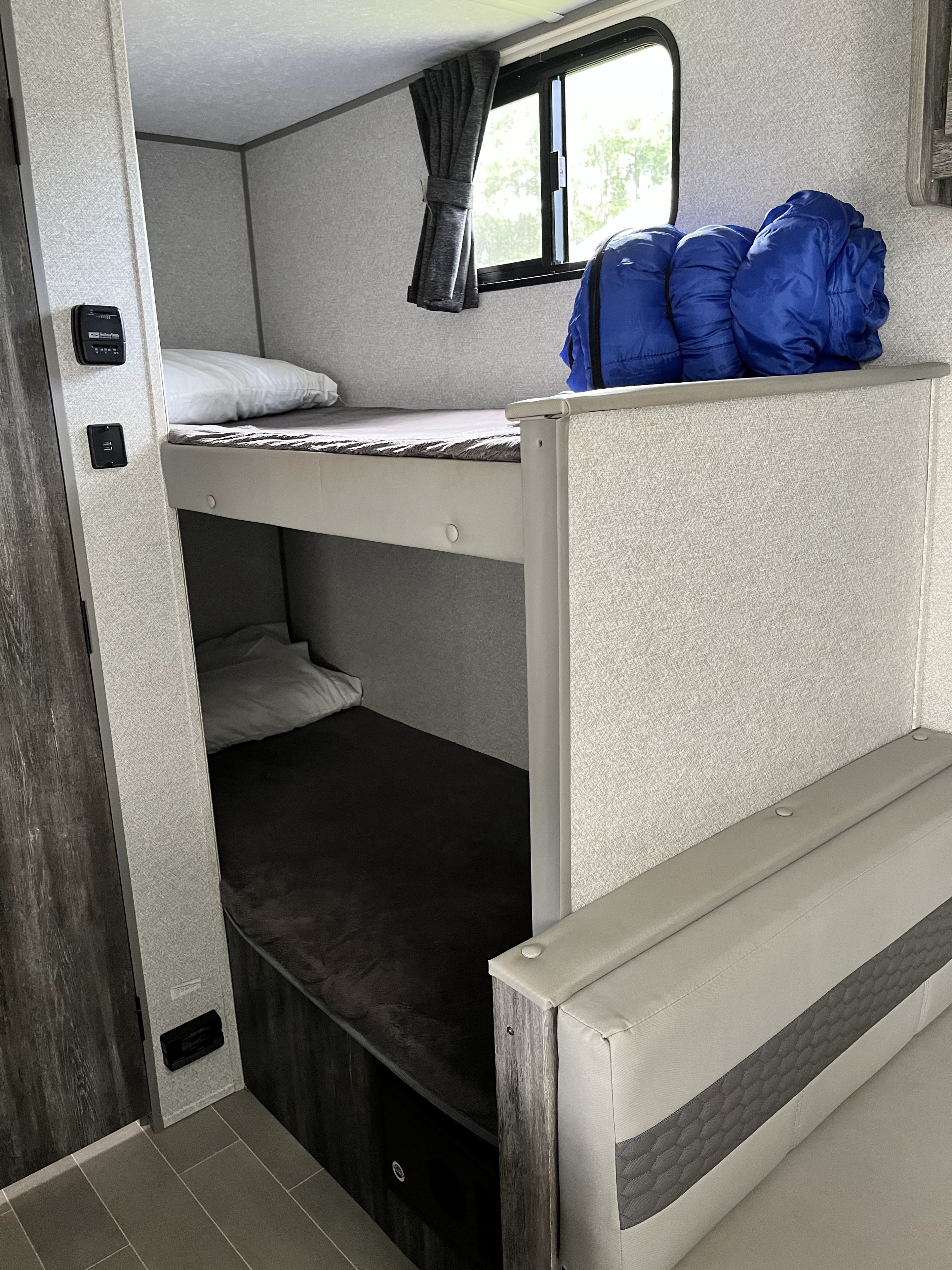 Inside an RV rental: cozy bunk beds with pillows, blue sleeping bags, a window, and climate controls.. Forest River Salem FSX PLATINUM 2020