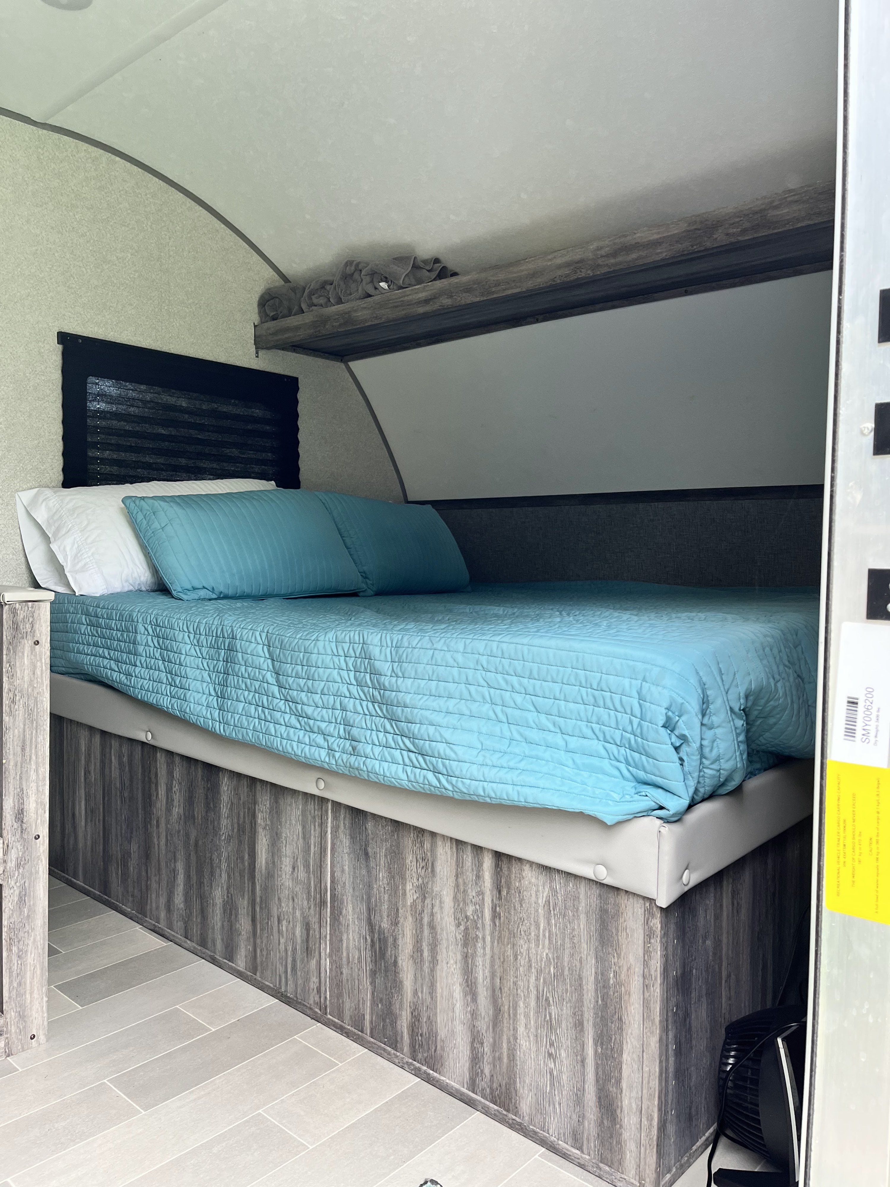 Compact RV rental bedroom with a blue bed, overhead shelf, and modern wood-look interior. Ideal for travel.. Forest River Salem FSX PLATINUM 2020