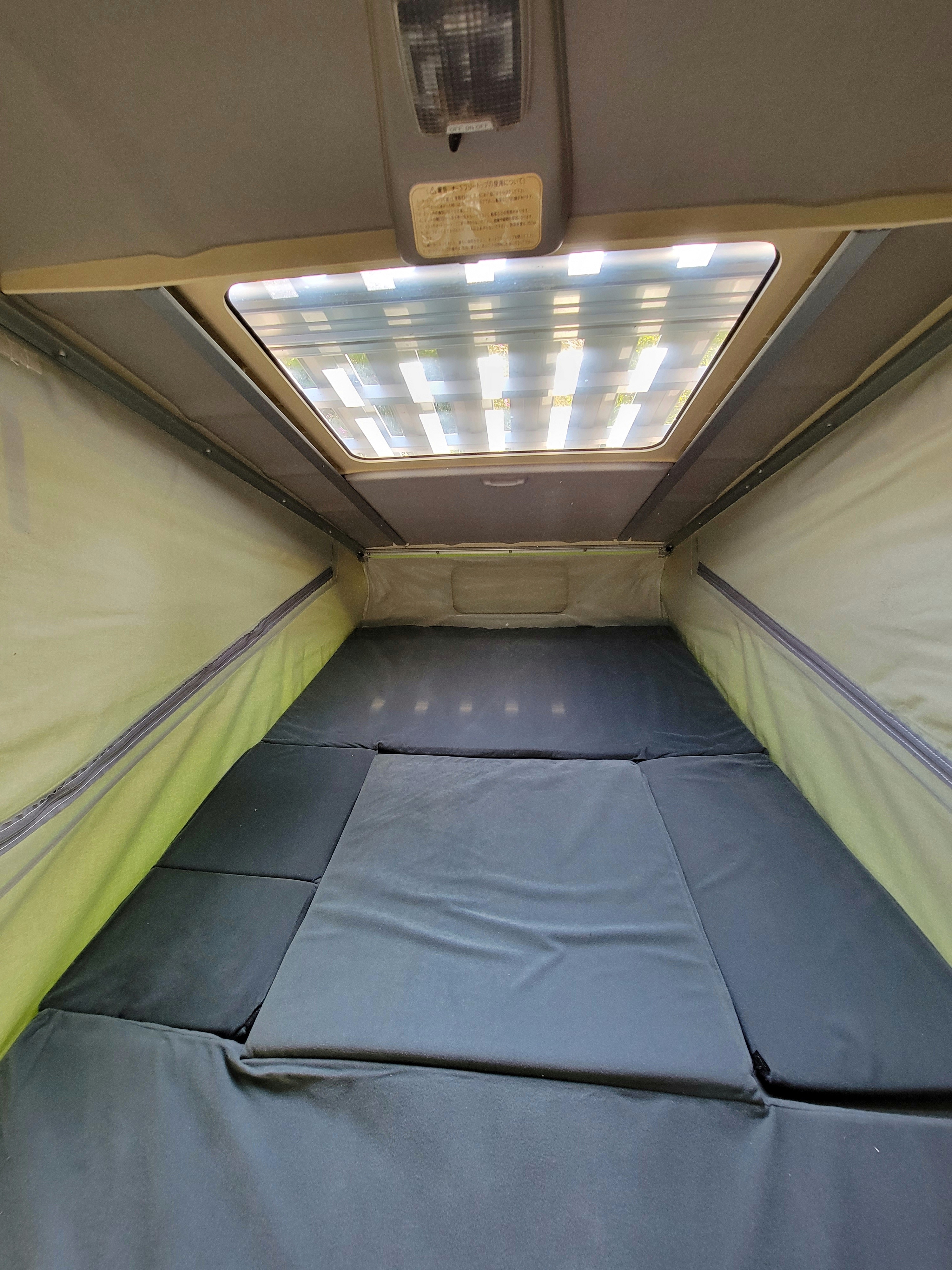 Inside an rv rental pop-top camper, this photo captures the comfortable sleeping area with dark mattresses & a skylight.. Mazda Campervan 1995