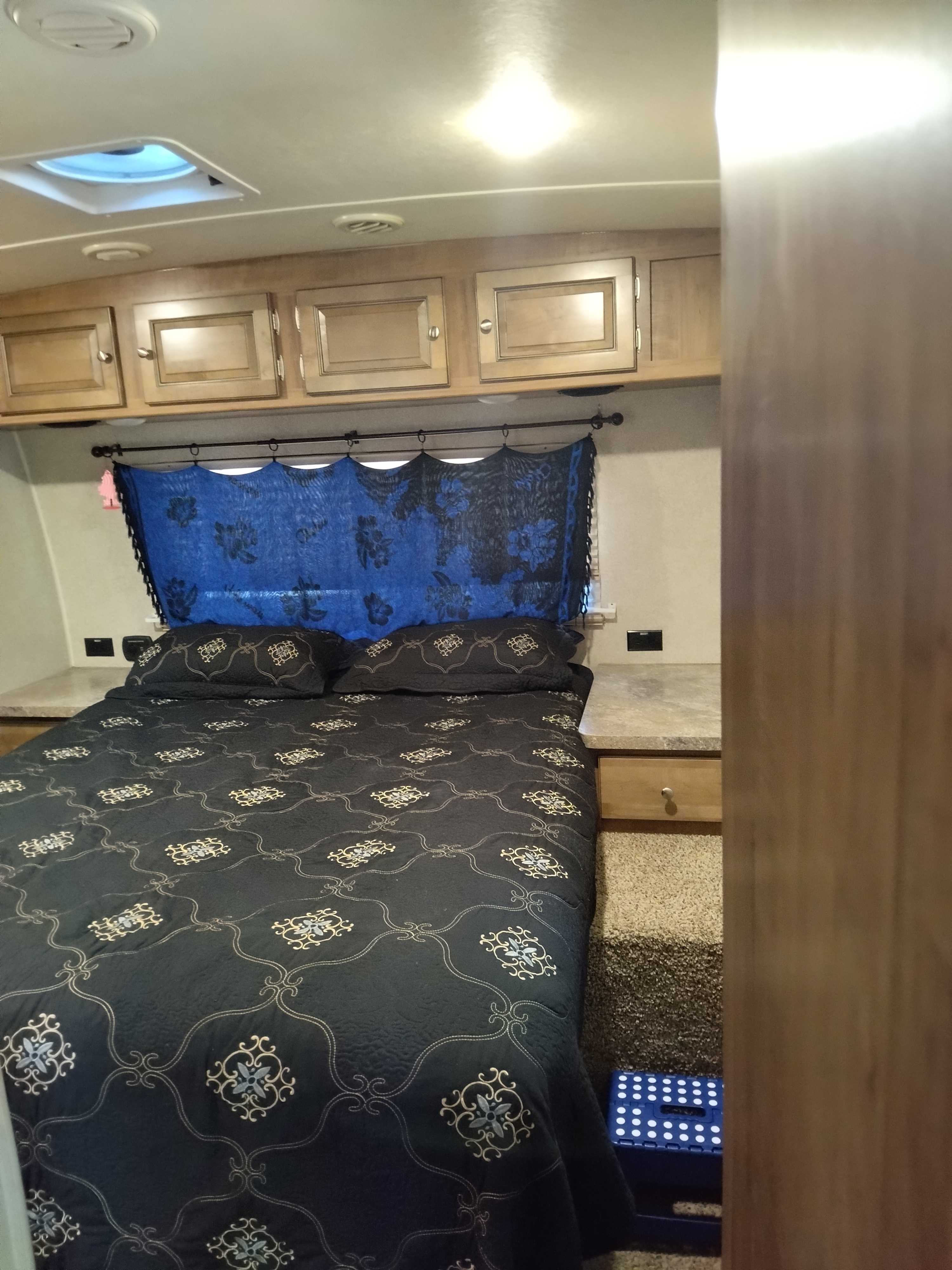 Cozy RV rental bedroom features a dark patterned bed, ample storage cabinets, and blue window fabric.. Forest River Rockwood Ultra Lite 2018