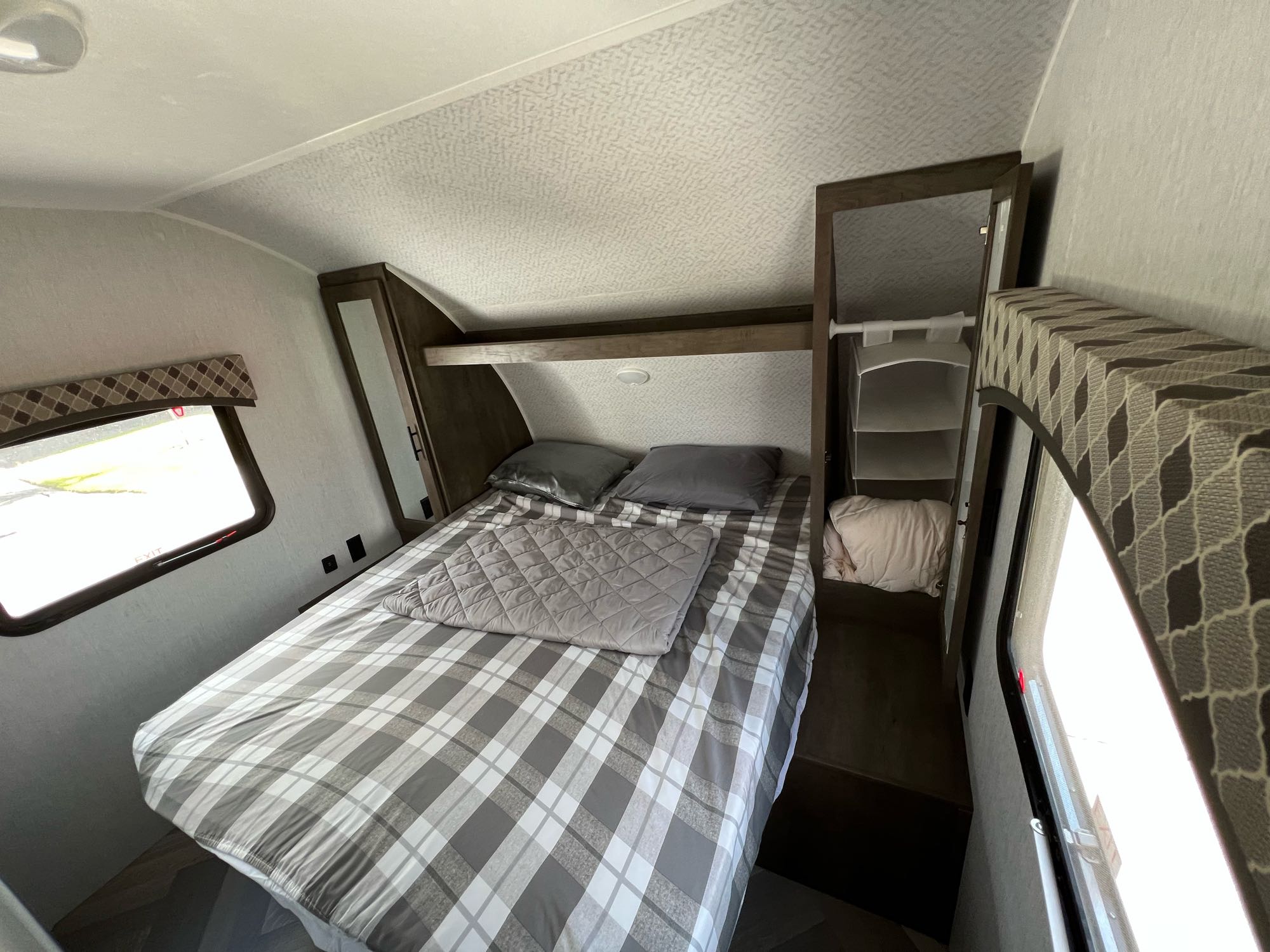 Cozy RV rental bedroom showing a plaid bed, built-in storage, and a large window with an 'EXIT' sign.. Forest River EVO 2700 BHX 2022