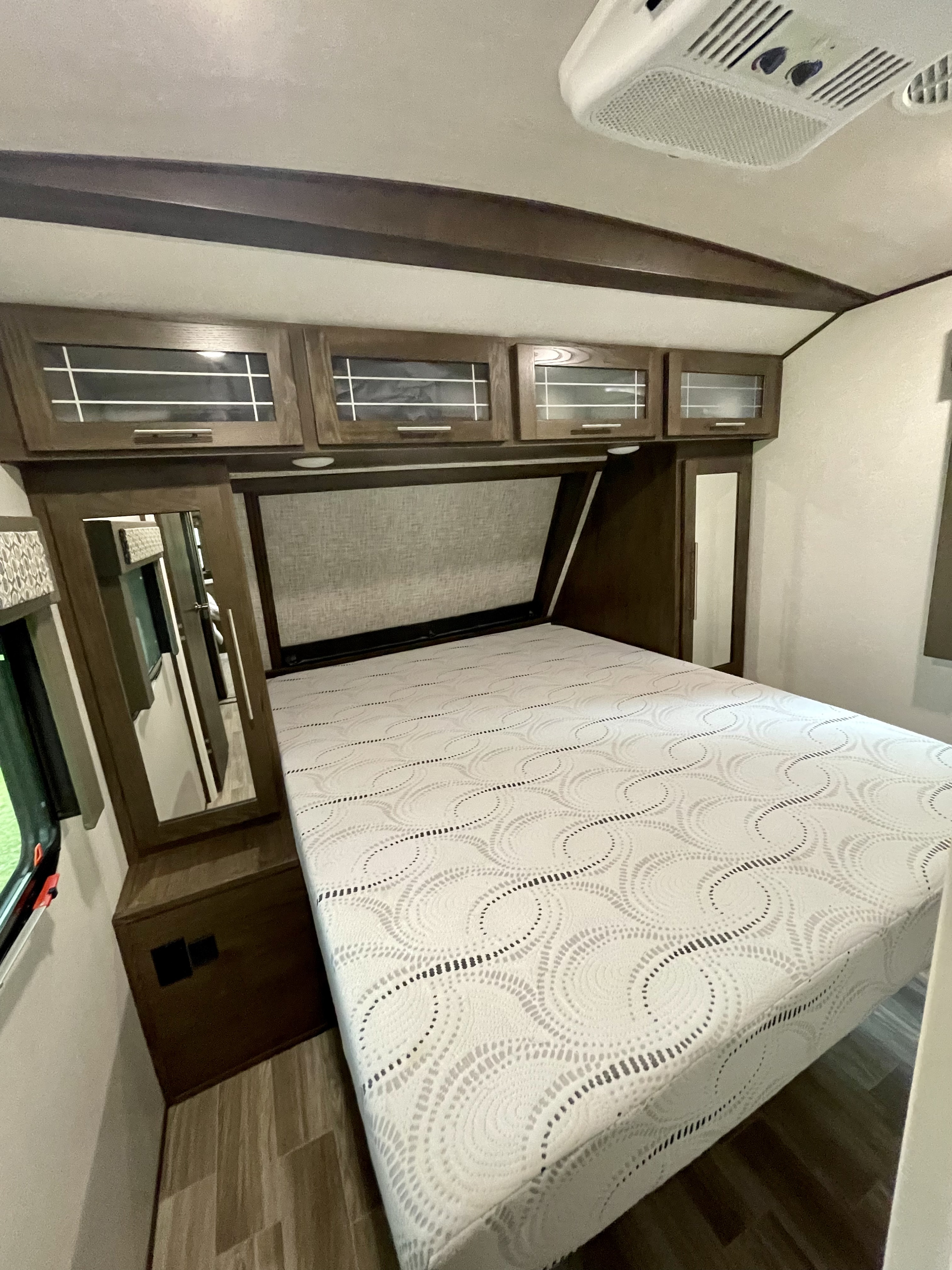 This RV rental bedroom features a comfy bed with patterned mattress, overhead cabinets, and a mirror.. Forest River Salem Hemisphere 2020