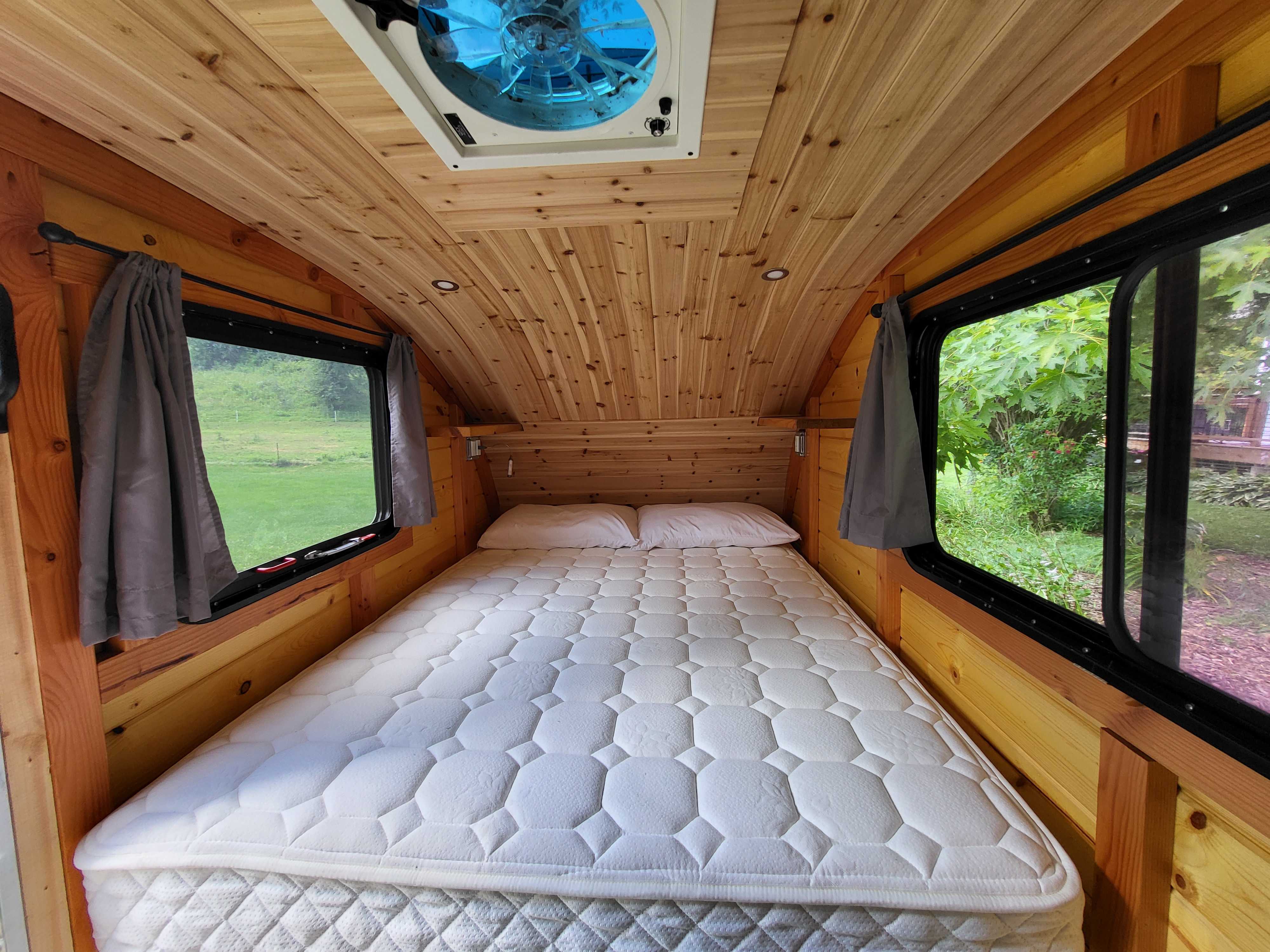 Cozy wood-paneled RV rental interior with a comfortable bed, windows, and a ceiling vent, perfect for outdoor adventures.. Custom Camper 2020