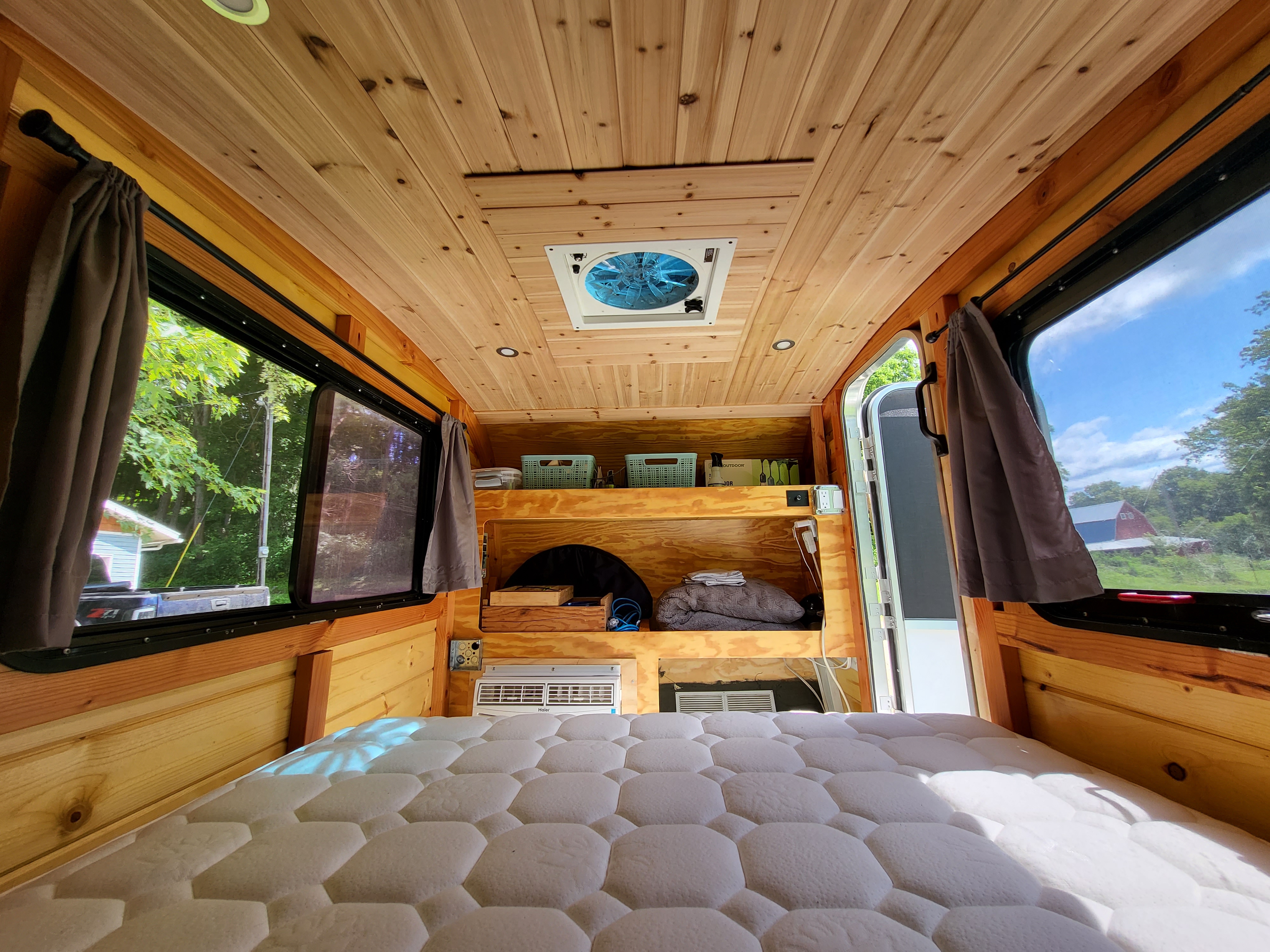 RV rental: Cozy camper van interior with wood paneling, quilted mattress, ceiling fan, and outdoor views. Ideal for travel.. Custom Camper 2020