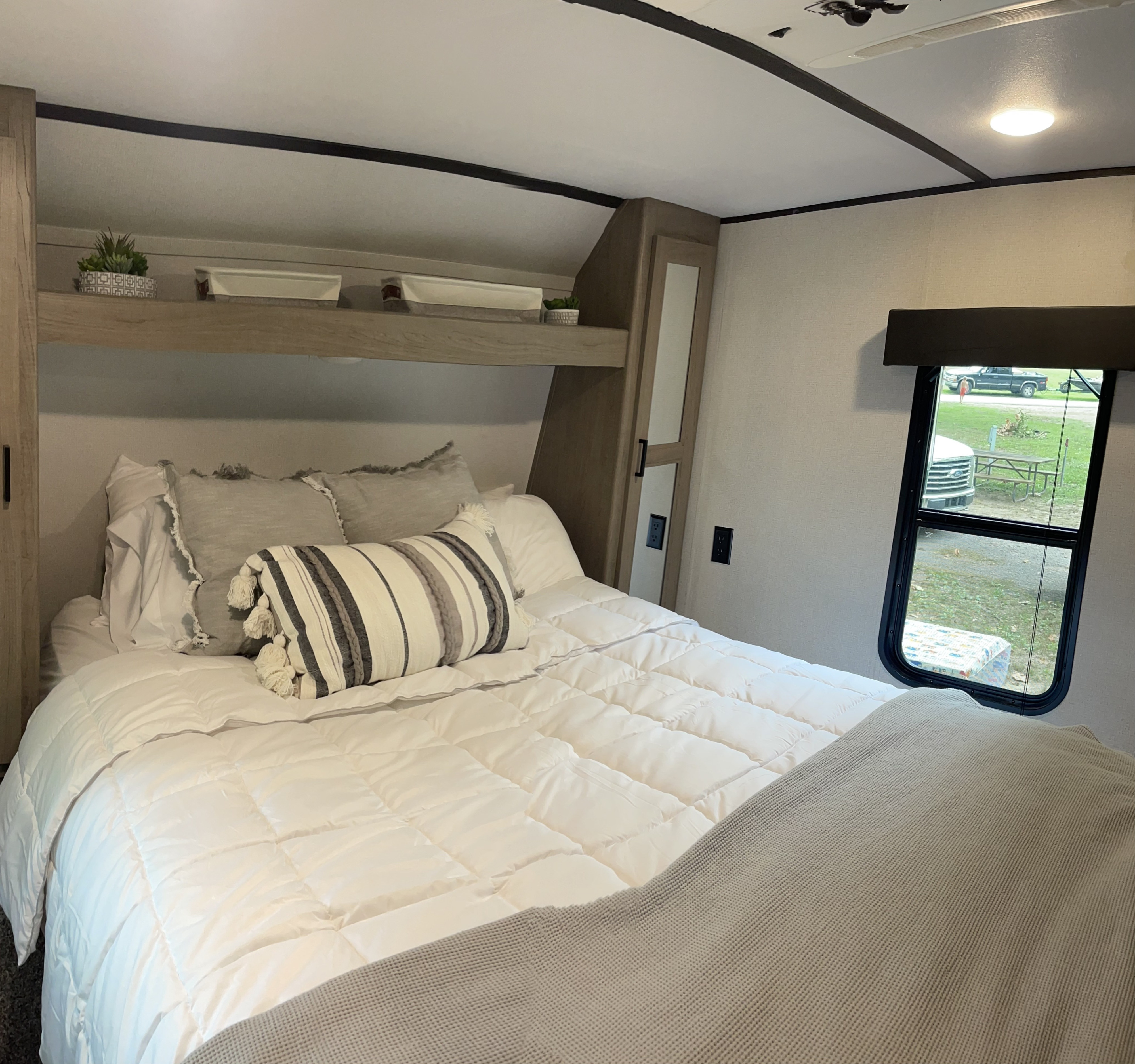Spacious RV rental bedroom featuring white bedding, overhead storage, and a scenic campsite view from the window.. Keystone RV Hideout 2021