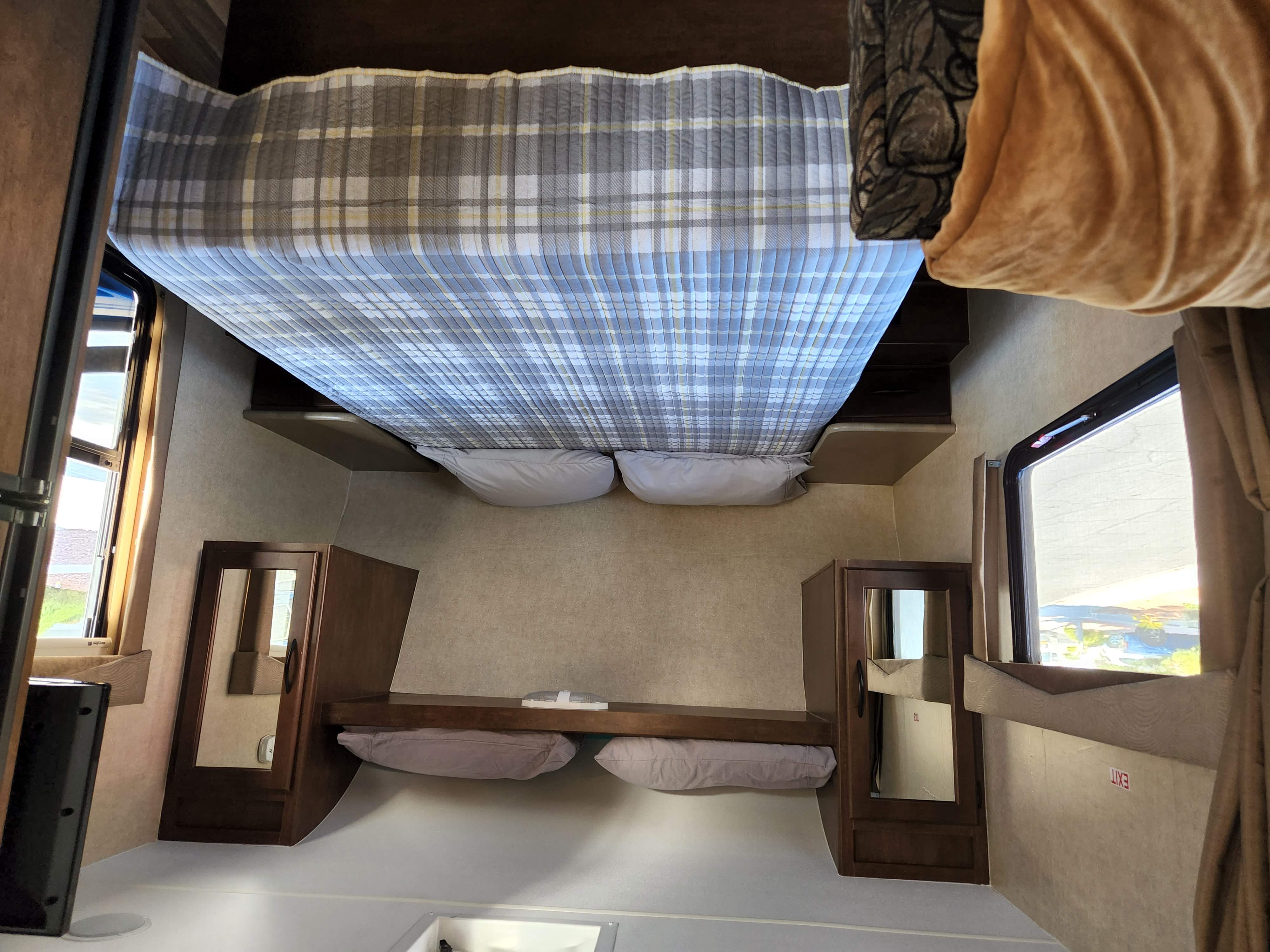 RV rental bedroom showcasing a plaid-patterned bed, soft pillows, and functional wood cabinetry beside windows.. Pacific Coachworks Tango Ultralite 2016