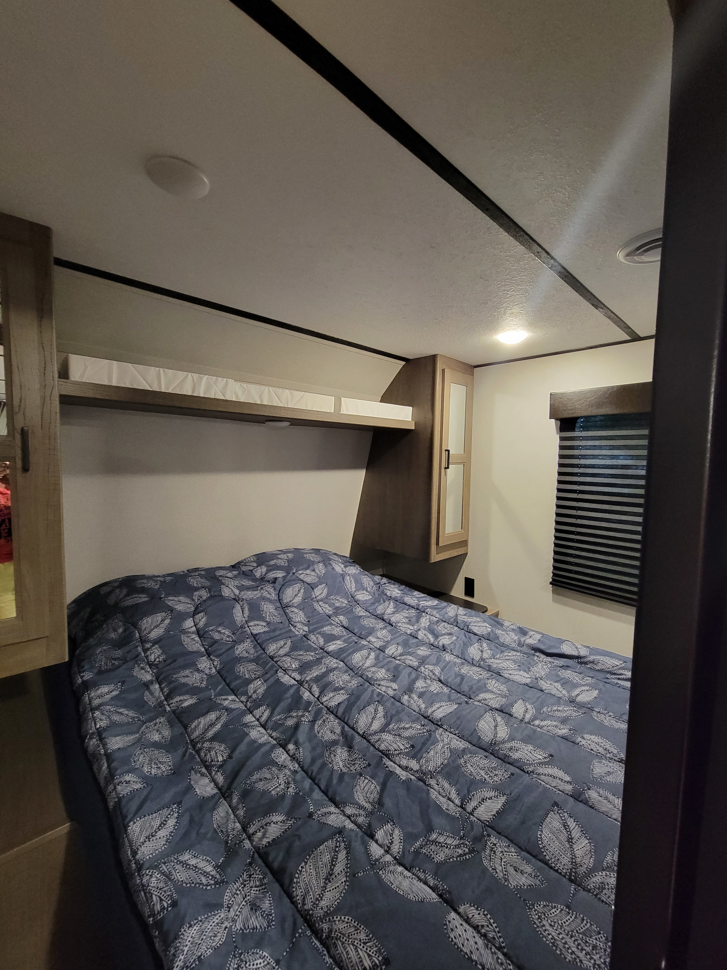 Compact RV rental bedroom, featuring a blue leaf-patterned bed, cabinets, and window blinds. Perfect for travel.. Keystone RV Hideout 2021